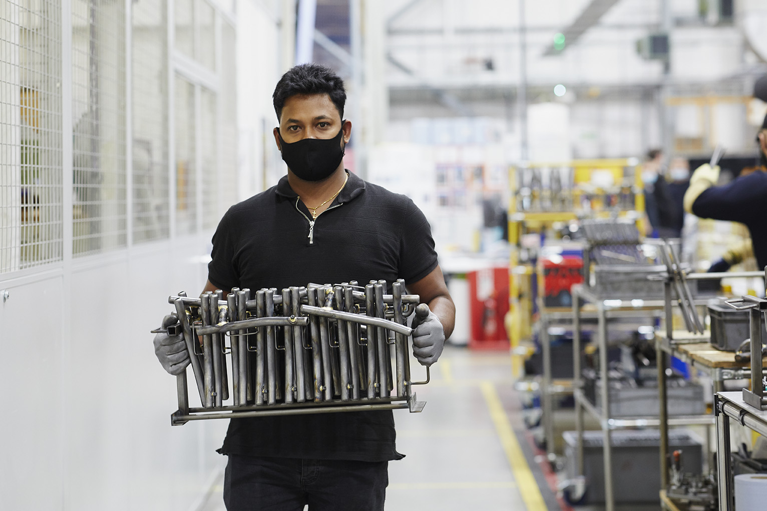 man in mask carrying componentry at brompton bicycle factory