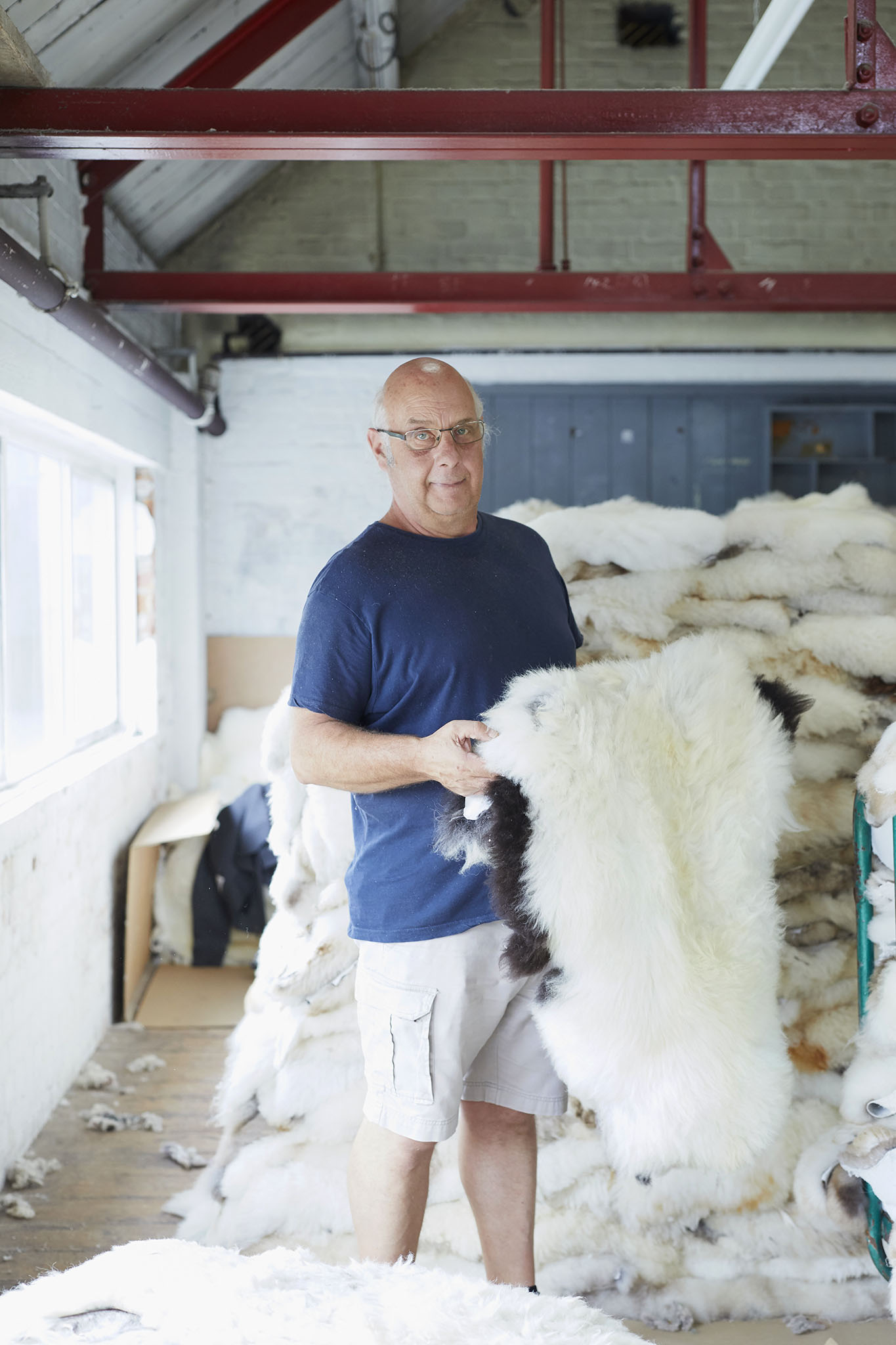 man holding sheepskin in factory with pile of sheepskins behind him devonia