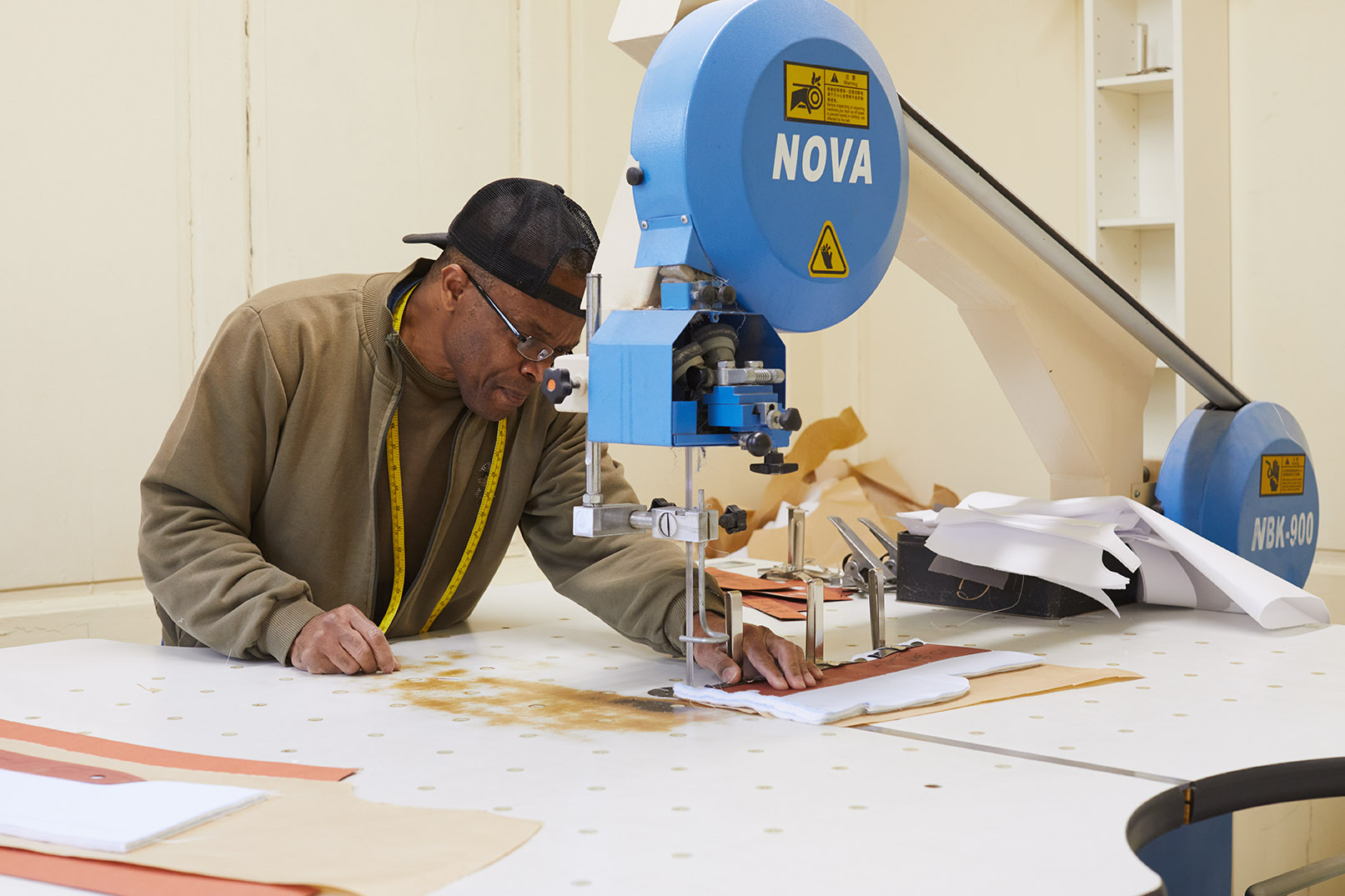 Emma Willis bespoke tailoring man in cap working at large sewing machine 