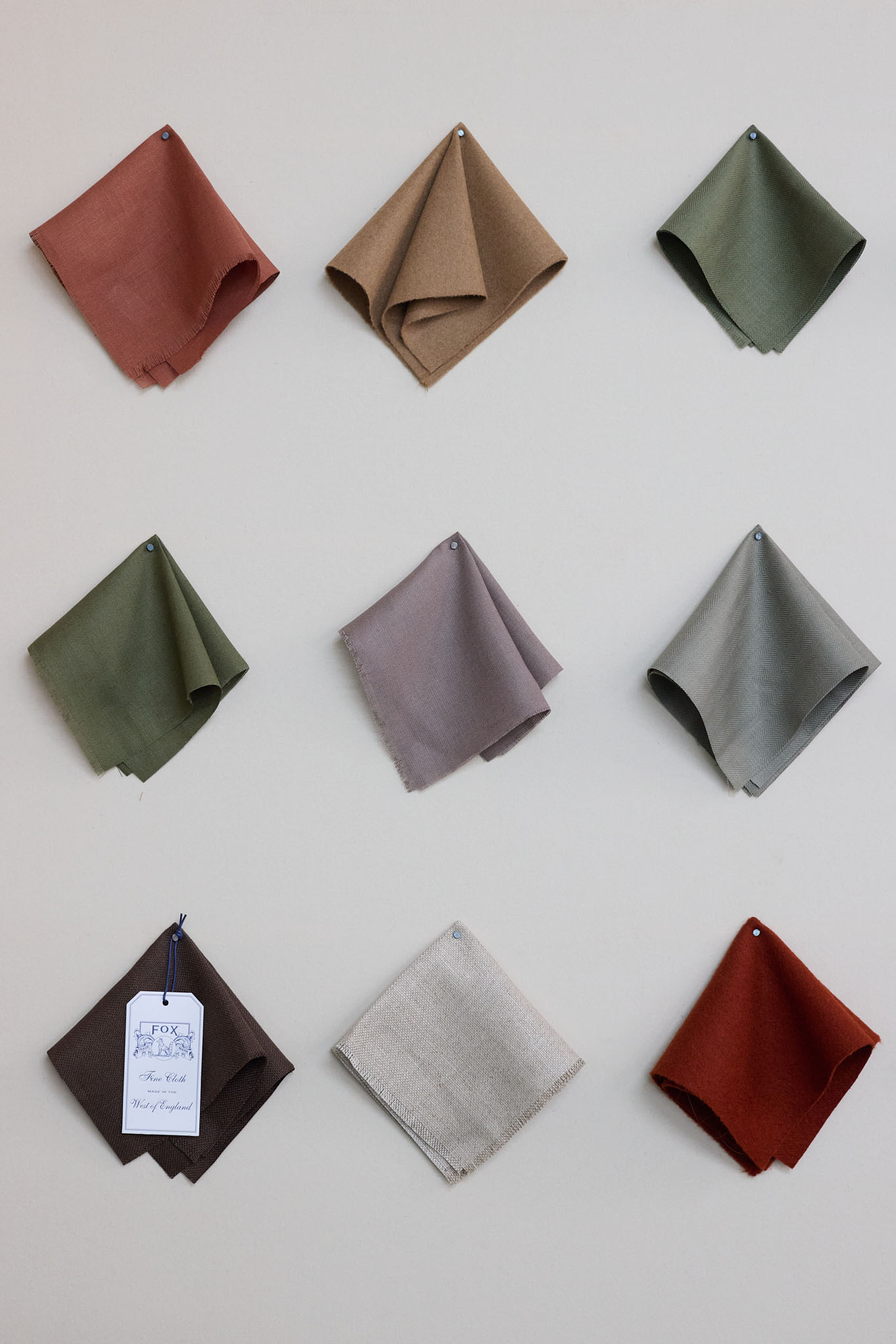 Fox Brothers white background with swatches if different colour fabric hung in threes wool cloth 