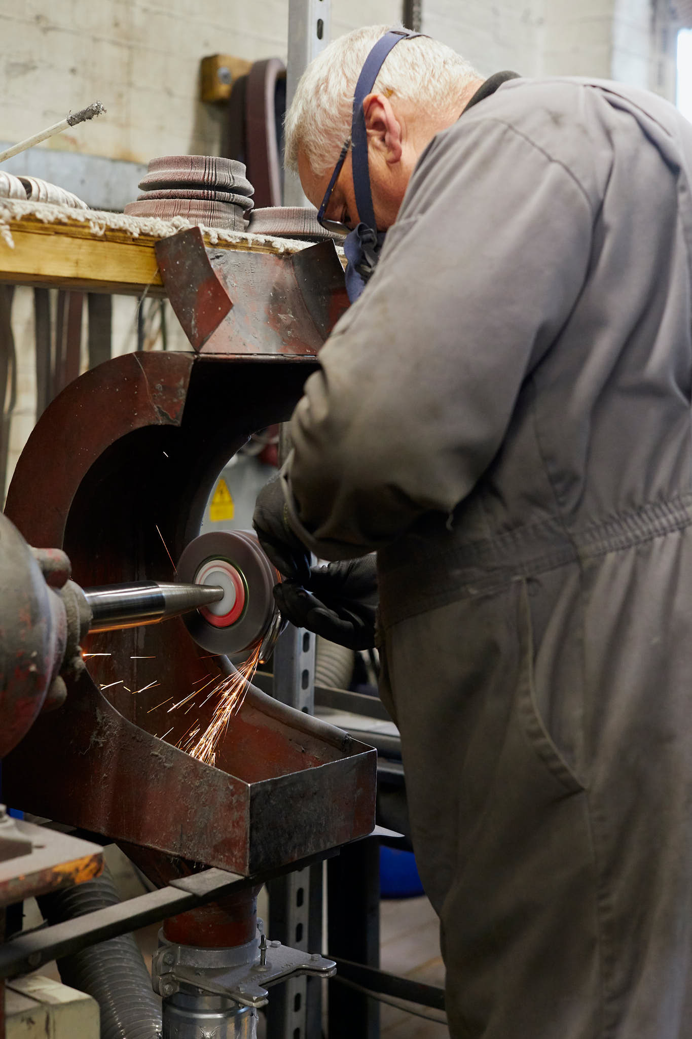 Ernest Wright man in black grey overalls and wearing protective mask standing at grinding wheel 