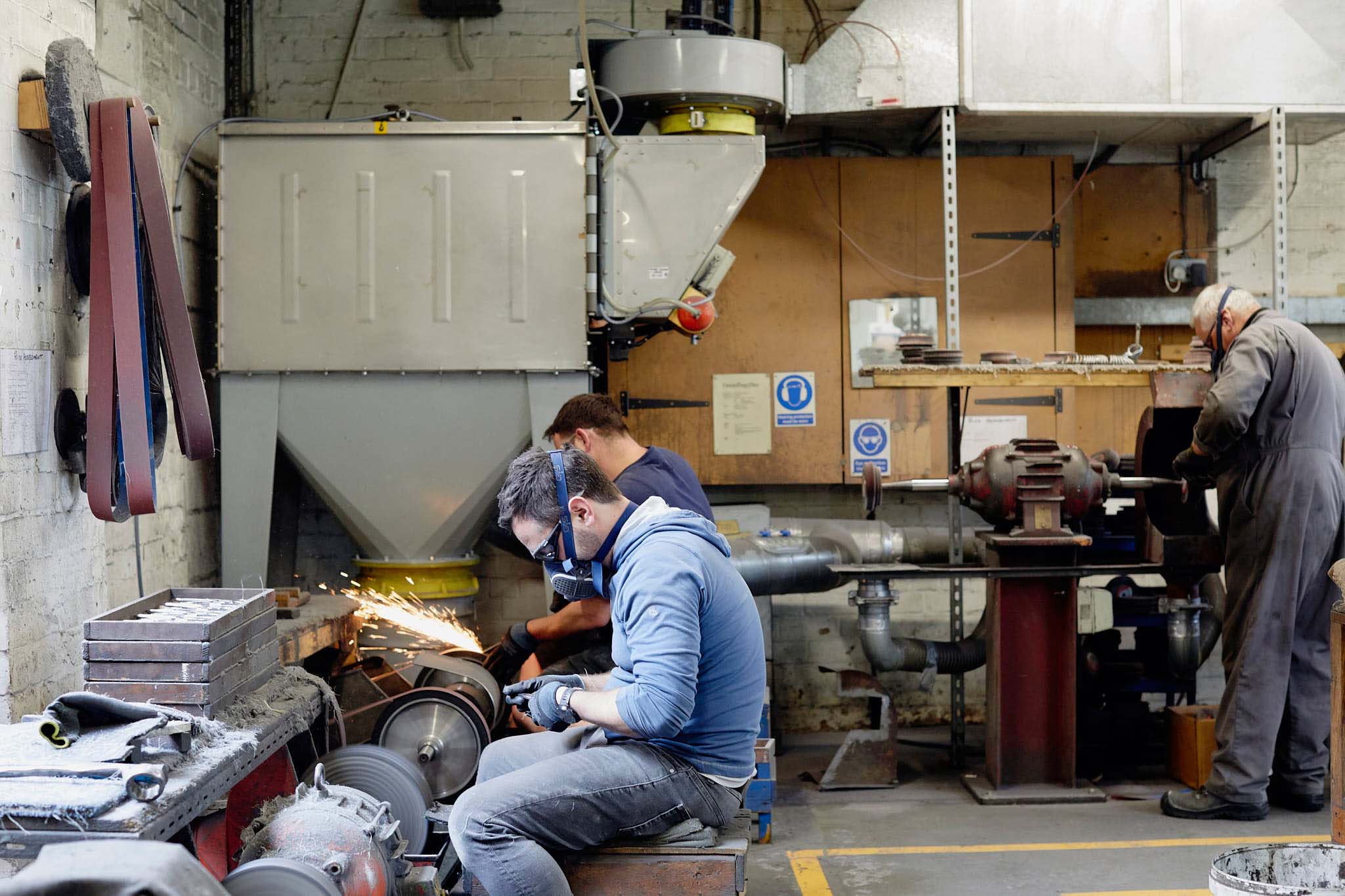 Ernest Wright men in workshop in blue overalls two are sitting at grinding wheels one is standing on the rights protective face gear blades