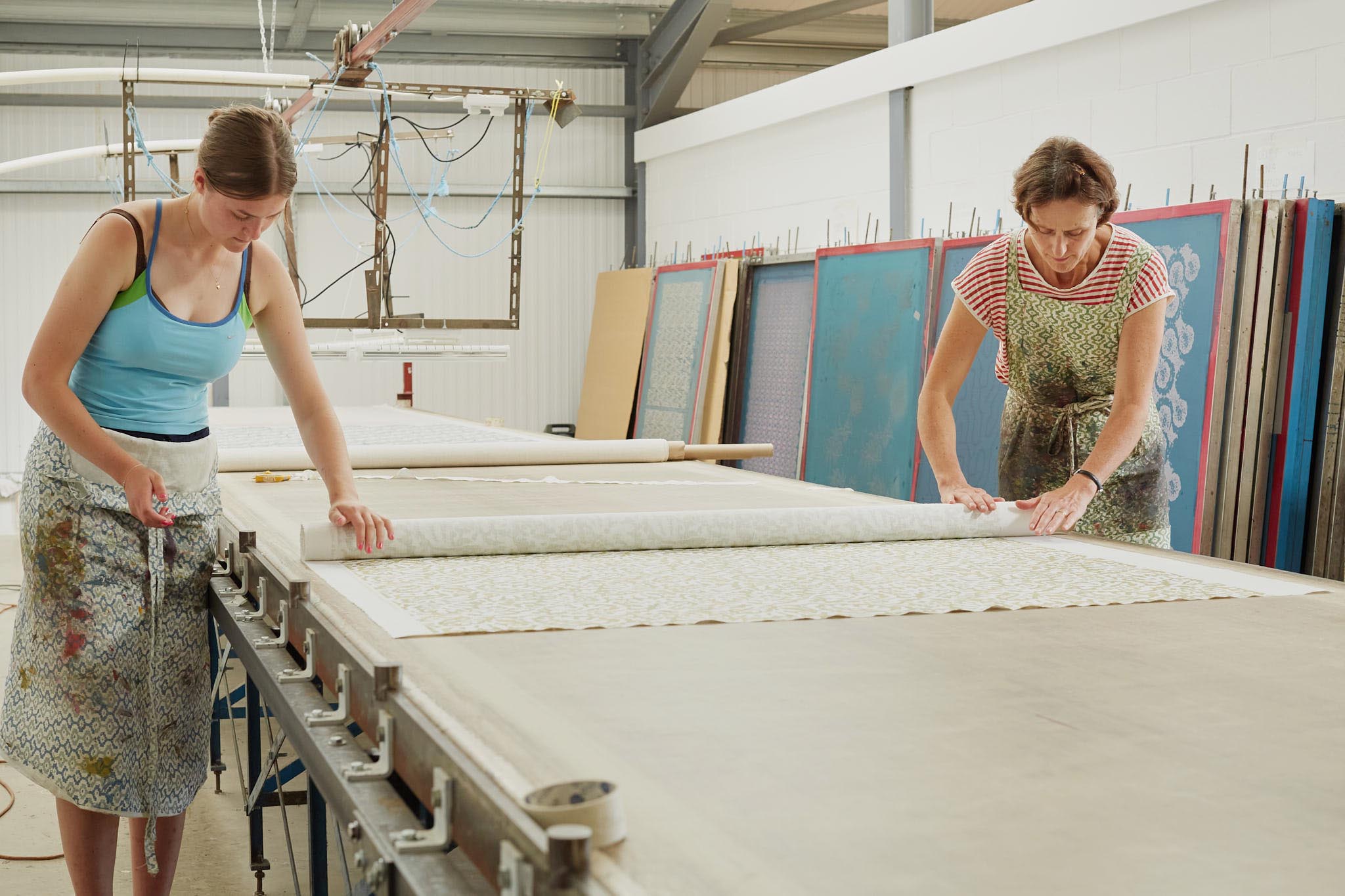 Rapture and Wright two women rolling out large roll of fabric on long table