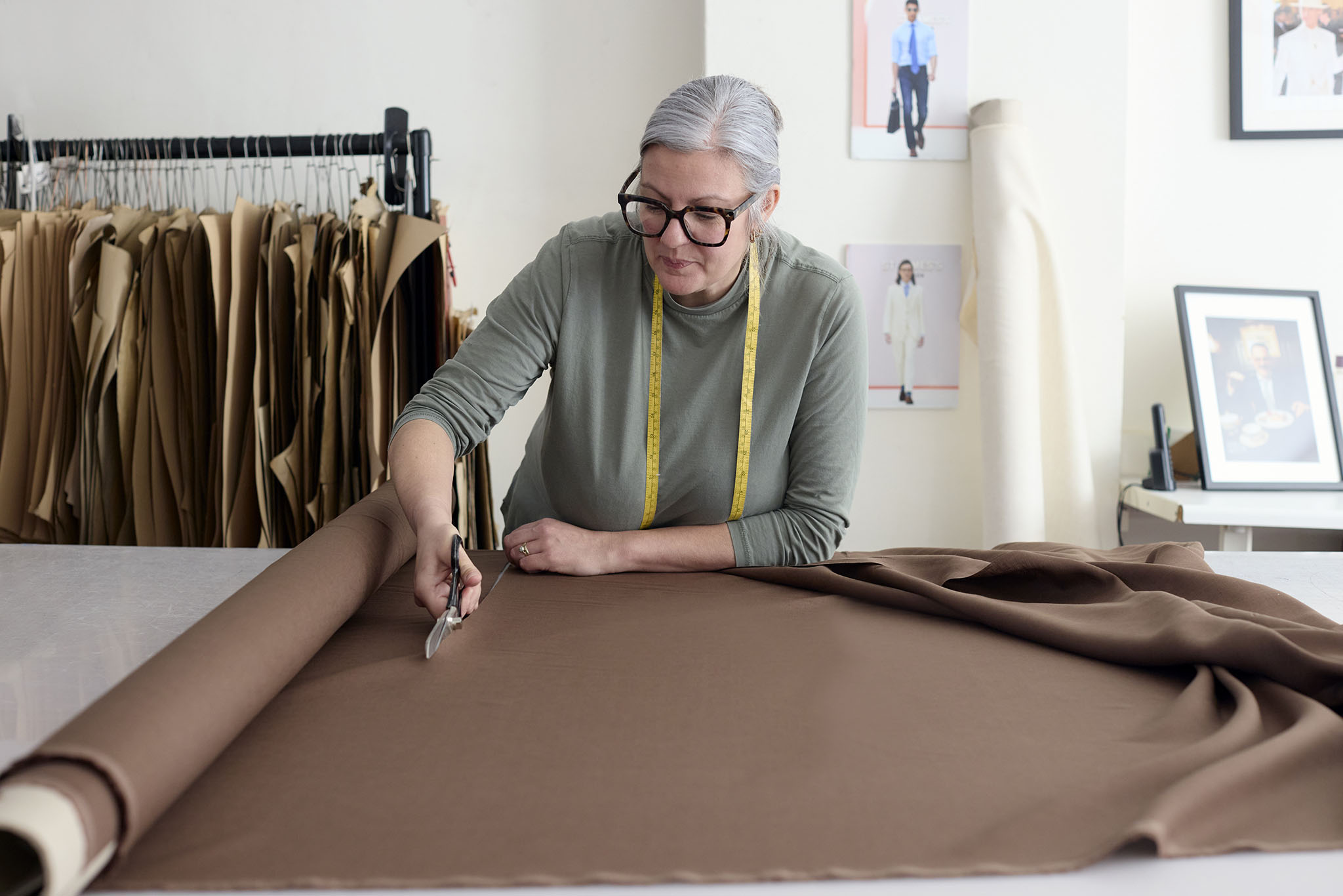 Emma Willis bespoke tailoring woman in glasses at worktable cutting from large roll of brown fabric