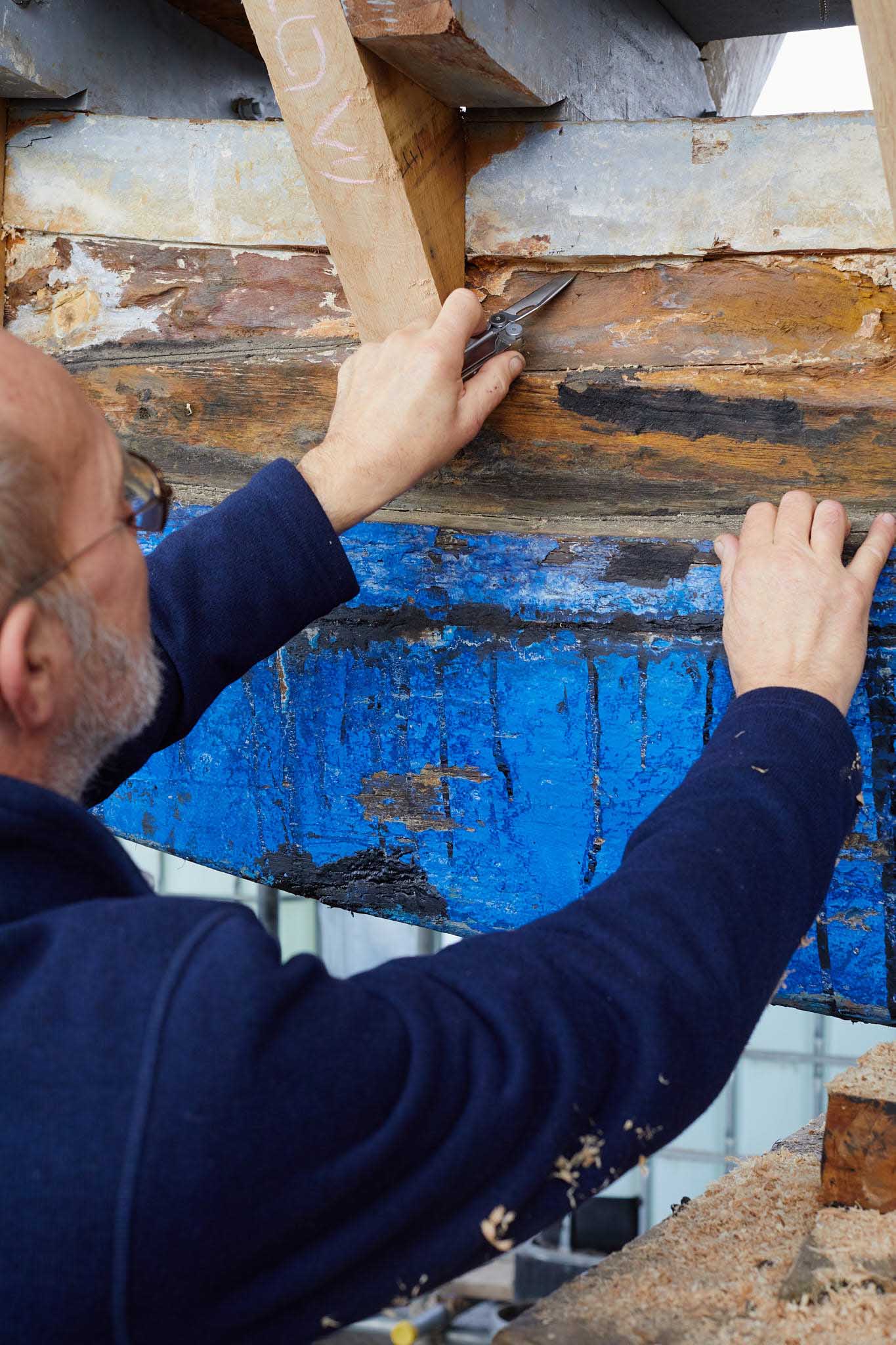 T Nielsen and Co man in blue overalls working on ship wooden hull