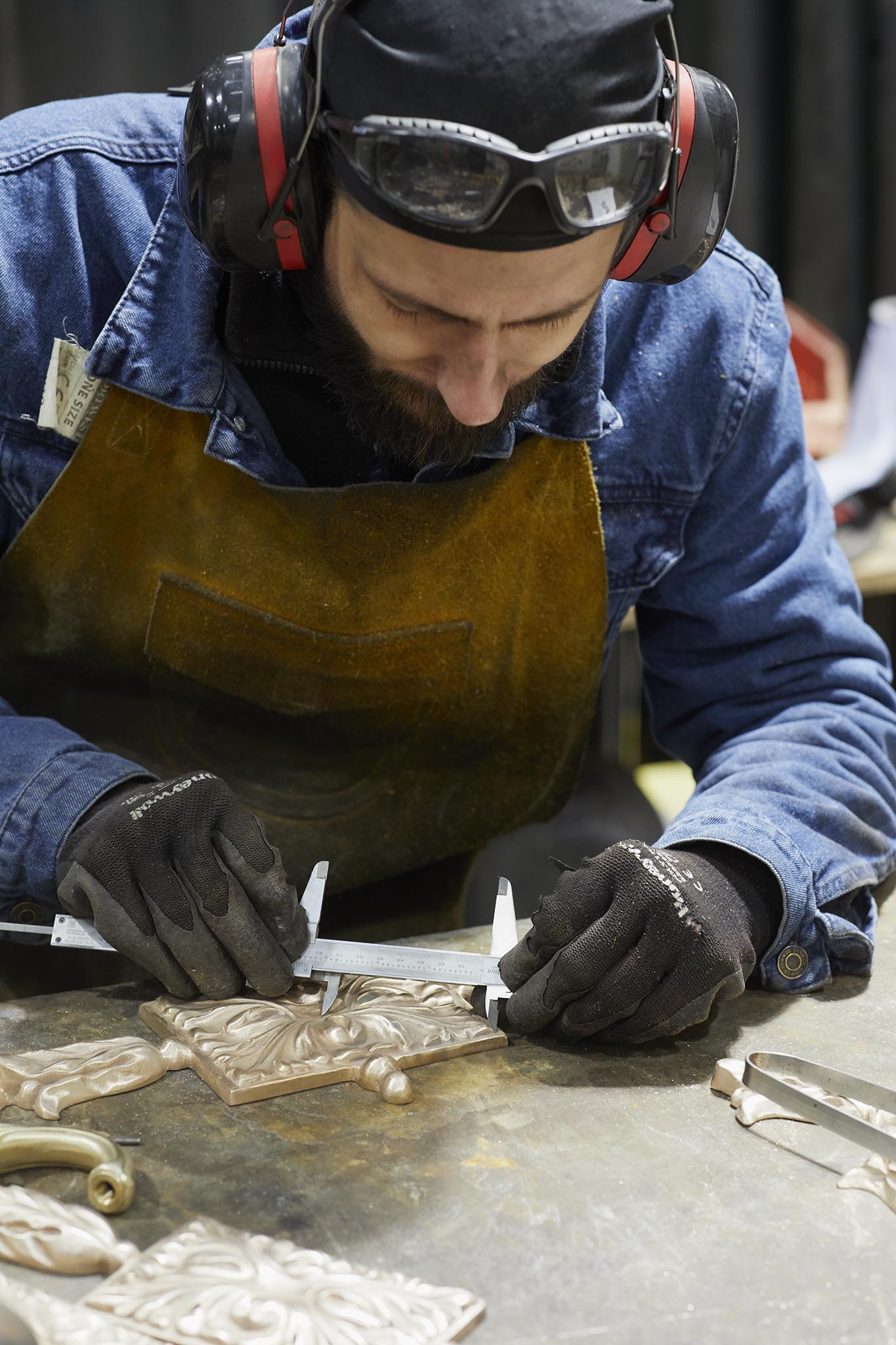 Cox London man in blue overalls and protective clothing working at table working with metal 