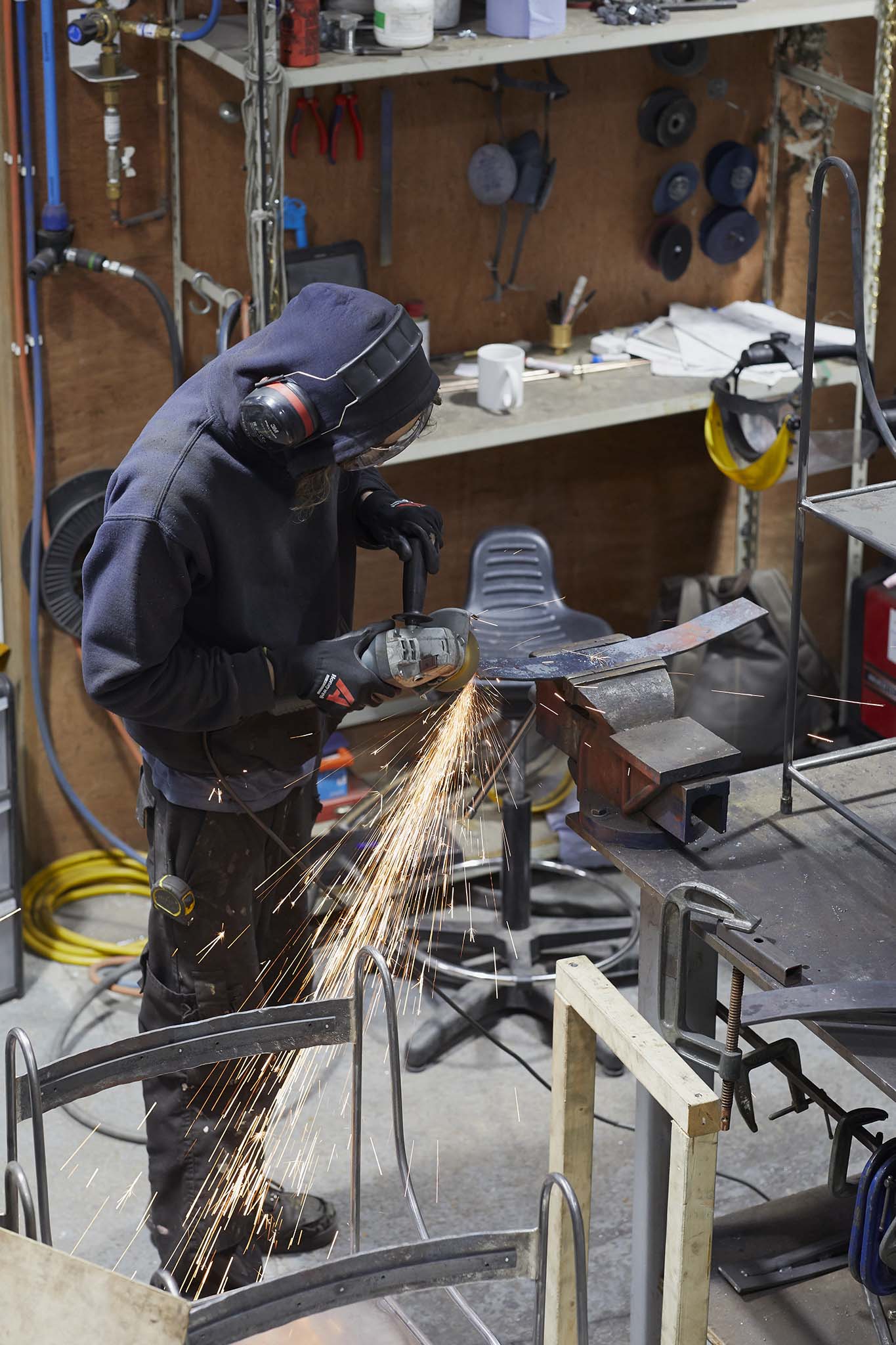 Cox London employee in protective clothing welding in workshop sparks are flying there are shelves in the background