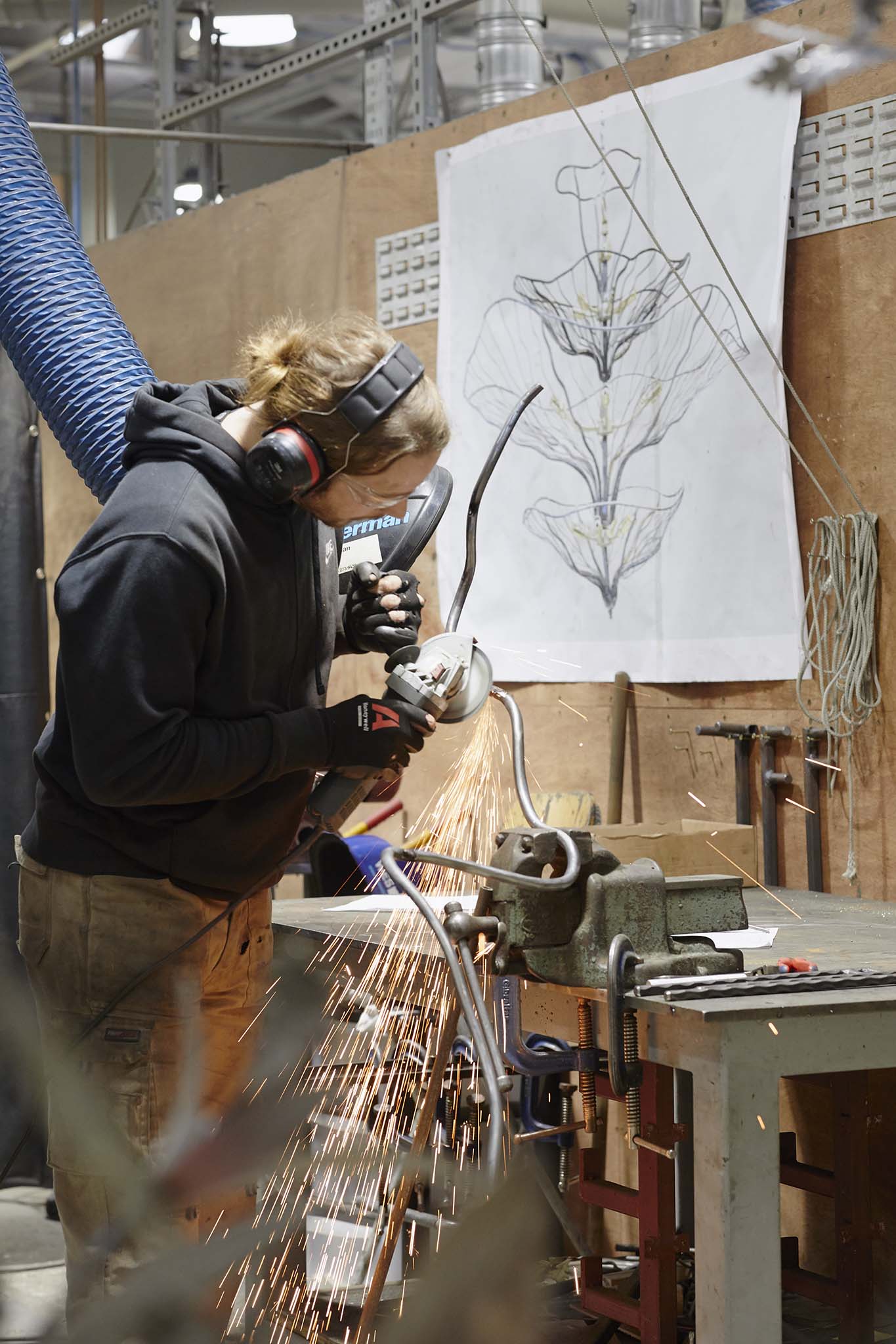 Cox London employee in workshop wearing protective clothing working with tools large white poster with line drawing design behind
