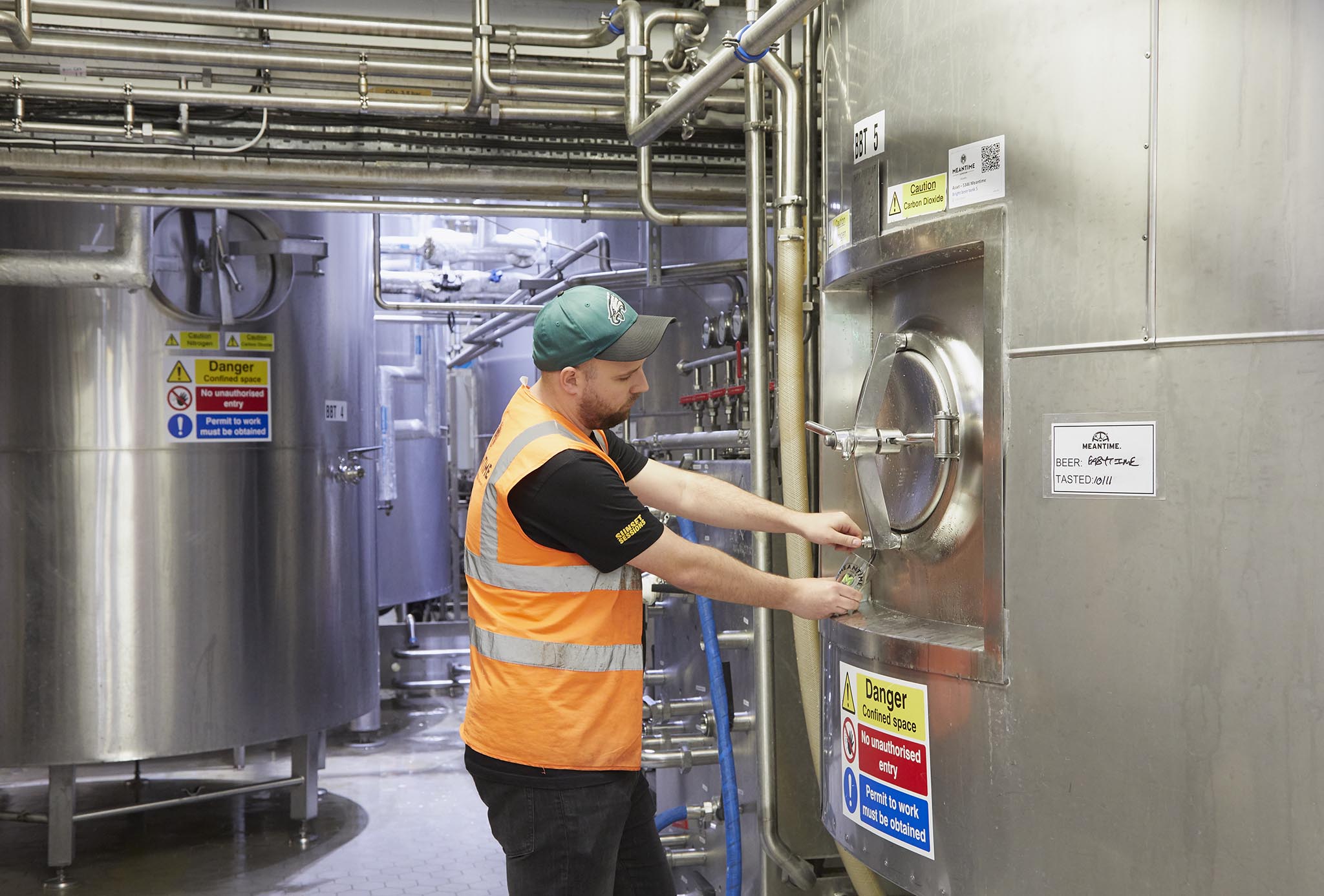 Meantime Brewing man in orange high vis jacket brewery factory opening large metal door warning signs