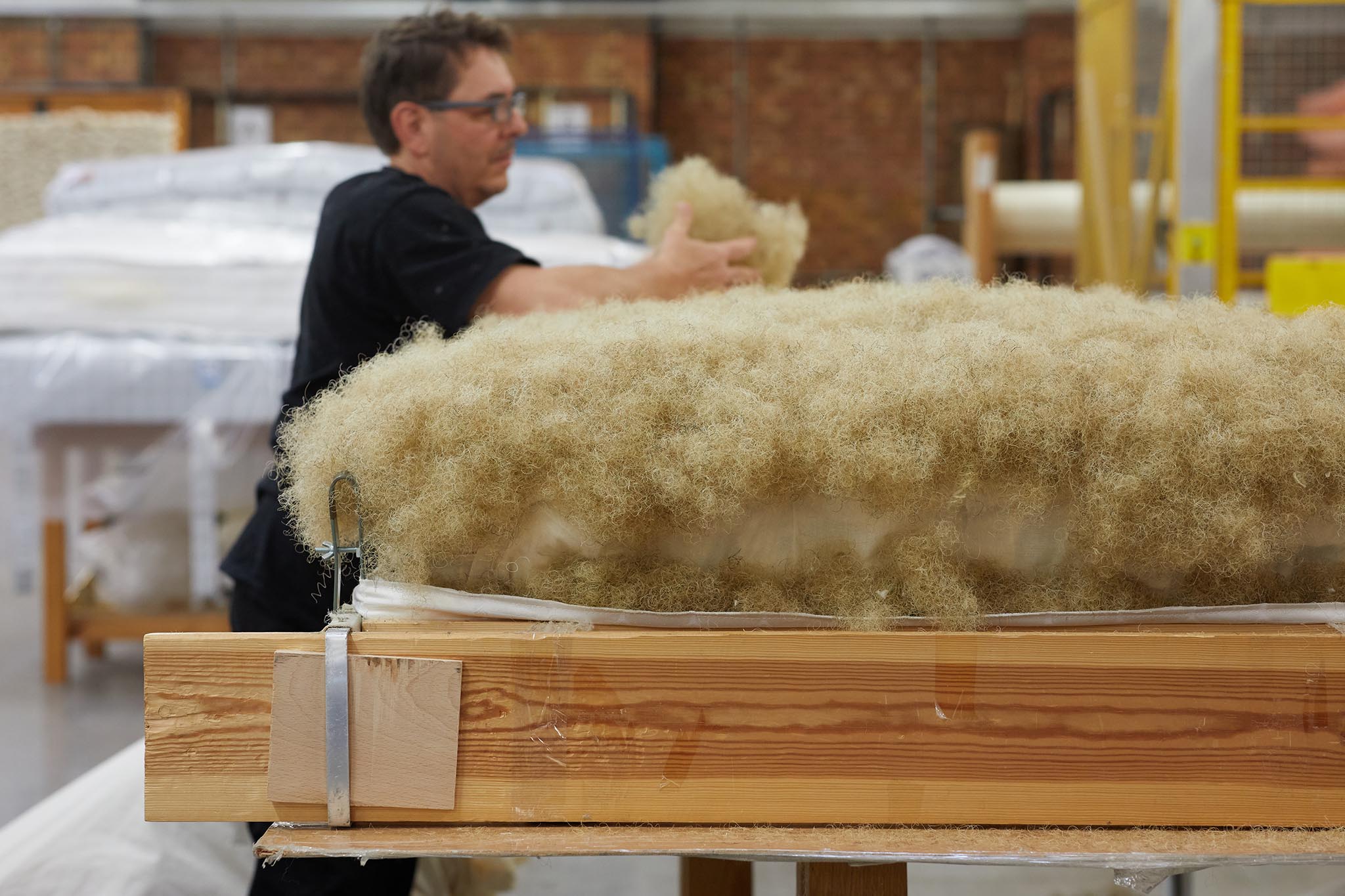 Savoir Beds wooden frame with yellow stuffing on top and man in black working in background 