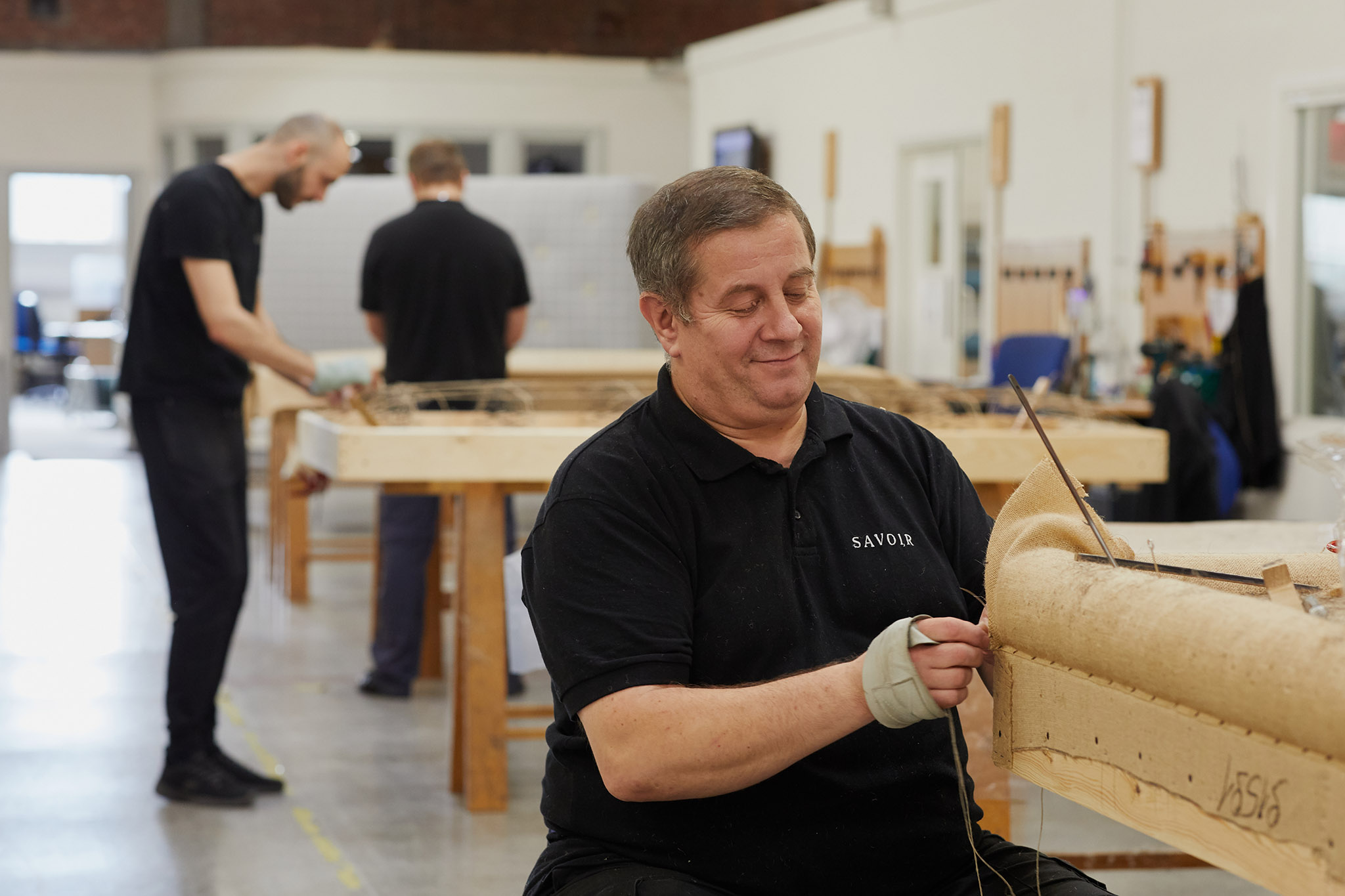 Savoir Beds men on workshop factory floor working on different stages of mattress construction pinning 