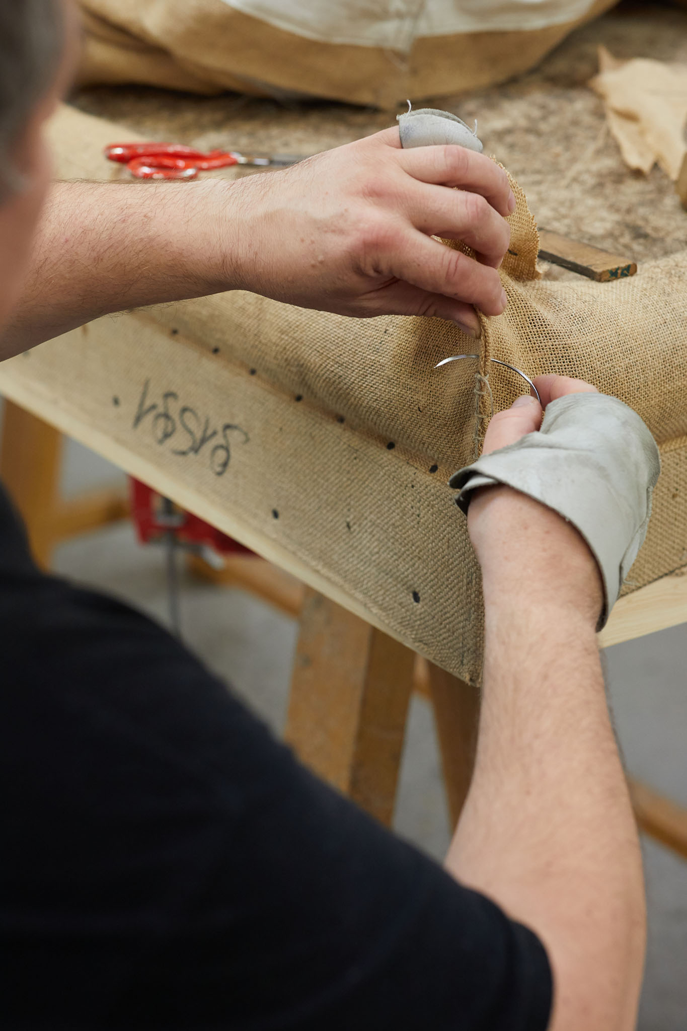 Savoir Beds man working on bed frame mattress cutting excess fabric on corner with scissors mattress filling spilling out of bag in background