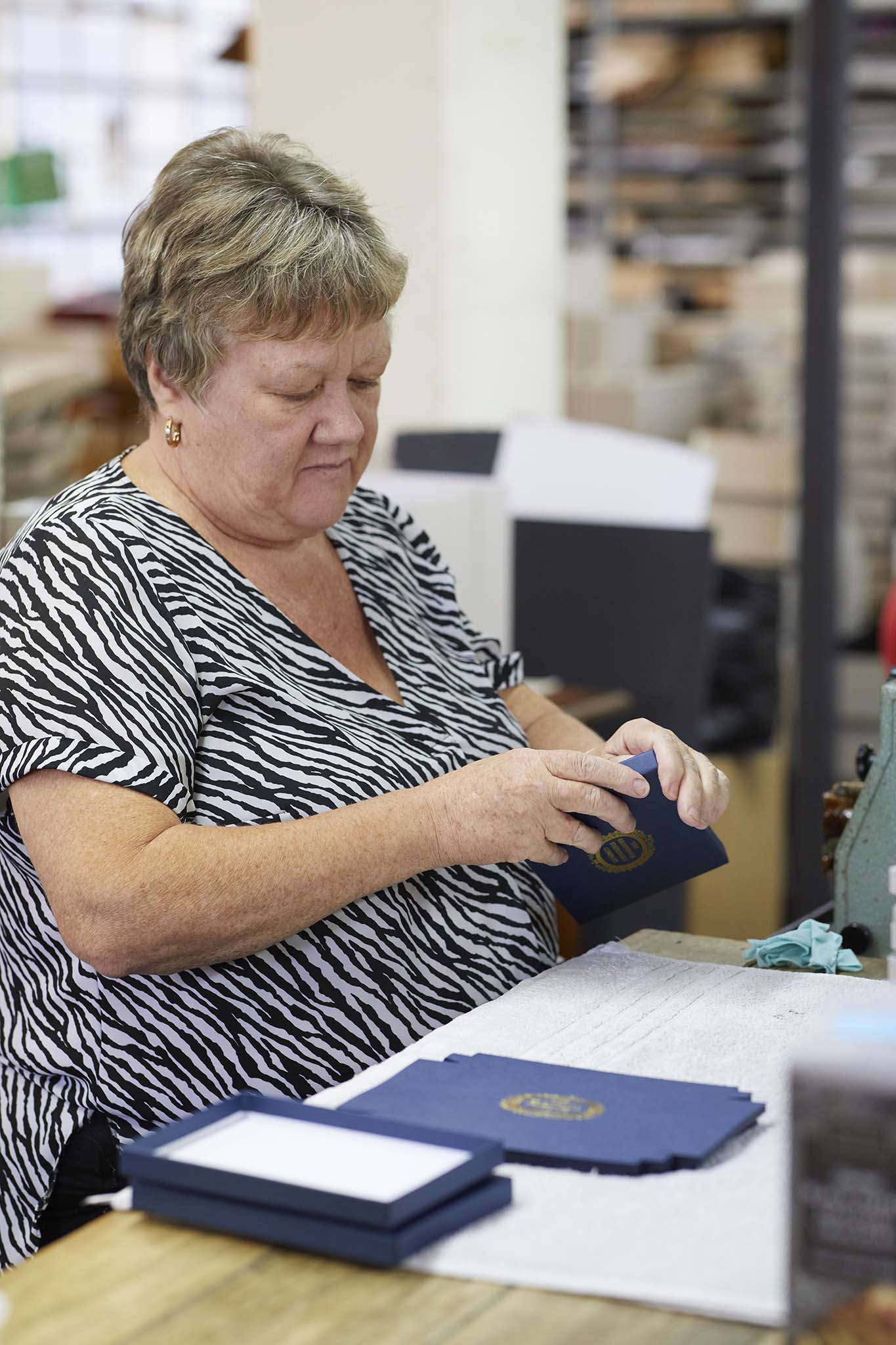 W MacCarthy & Sons woman assembling smart navy blue presentation box envelope sitting at table zebra print shirt