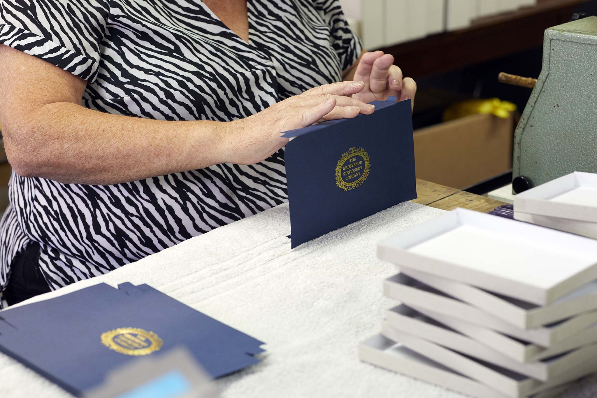 W MacCarthy & Sons woman assembling smart navy blue presentation box envelope sitting at table zebra print shirt