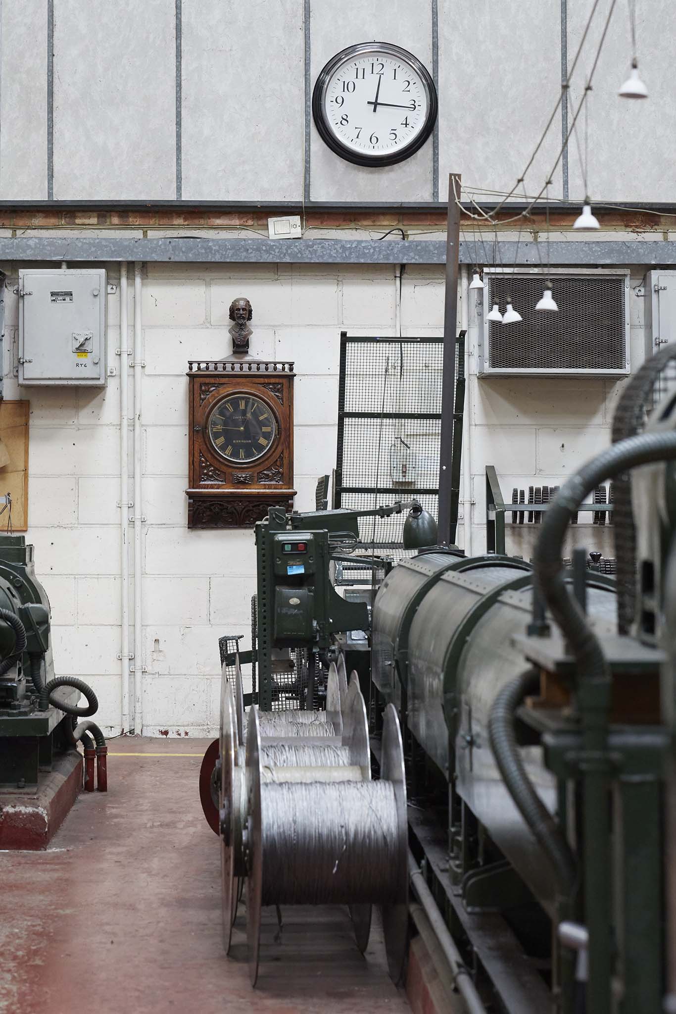 Ormiston Wire inside factory building white brick wall in background with clock on wall and large black machinery on factory floor