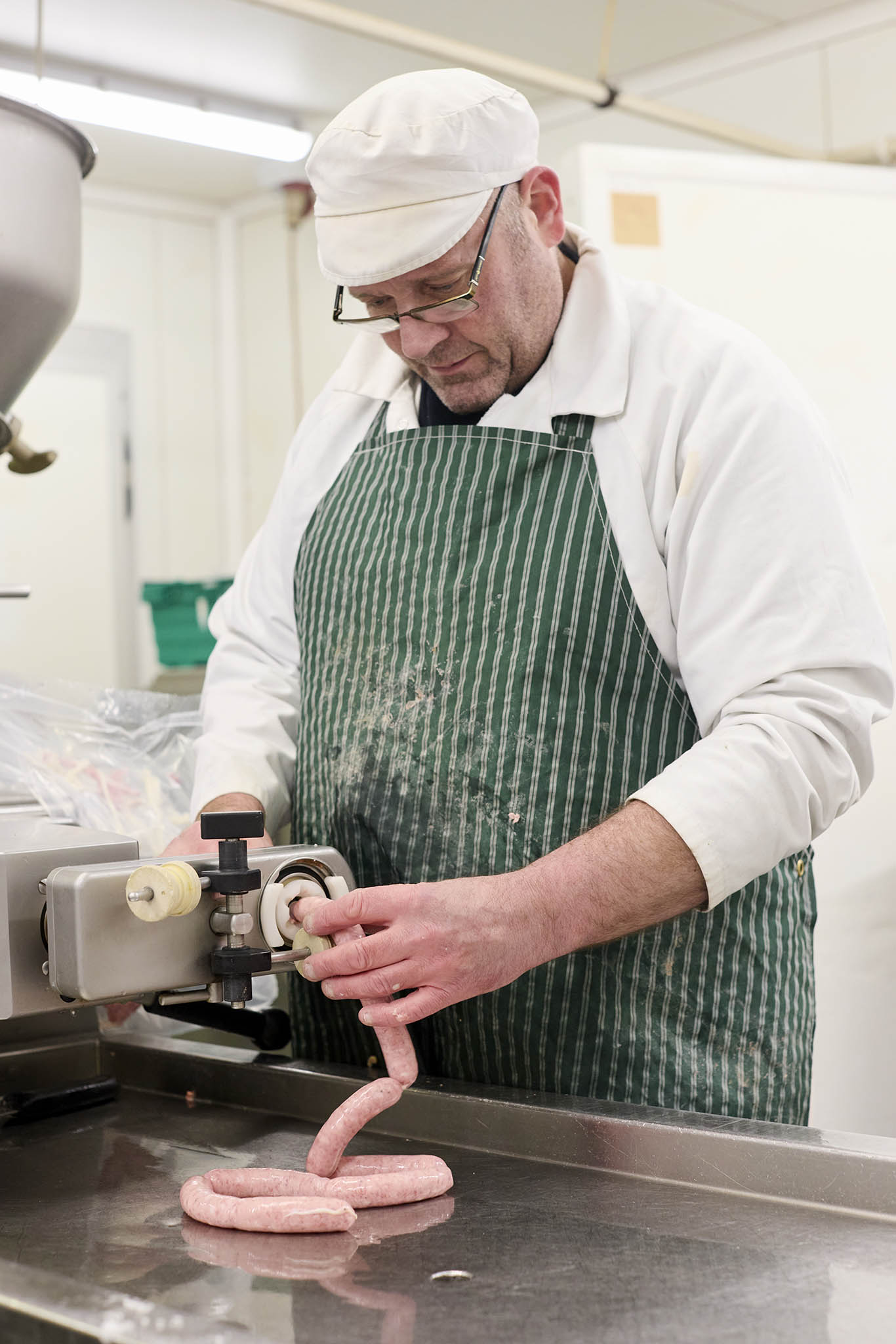 Swaledale Butchers working making filling sausages he is wearing white clothing and green apron