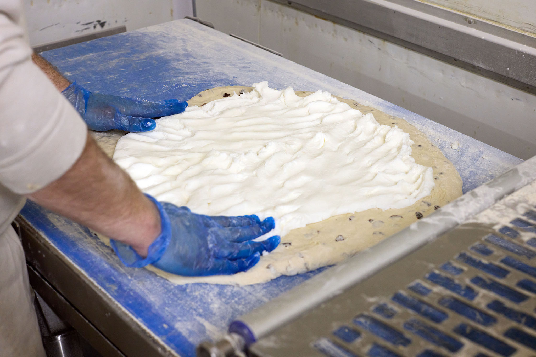 Janes Pantry bakers hands in blue gloves working with bread dough on stainless steel tray
