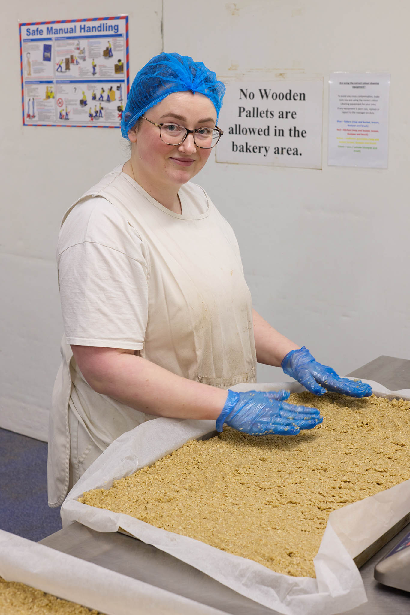 Janes Pantry employee baker in blue hair net smoothing out baked cake of pastry on a tray