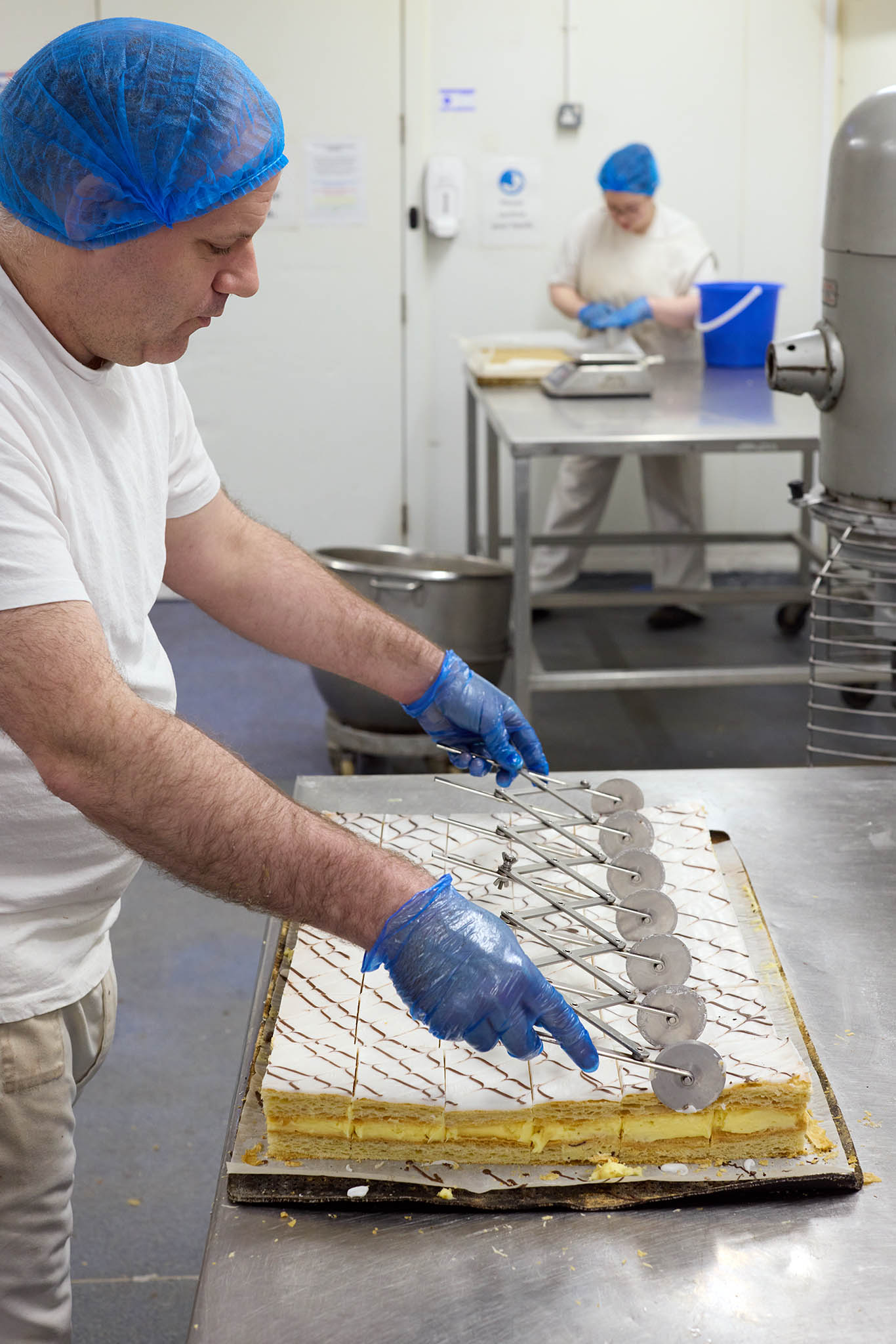 Janes Pantry employee baker cutting tray of finished cakes into portions 