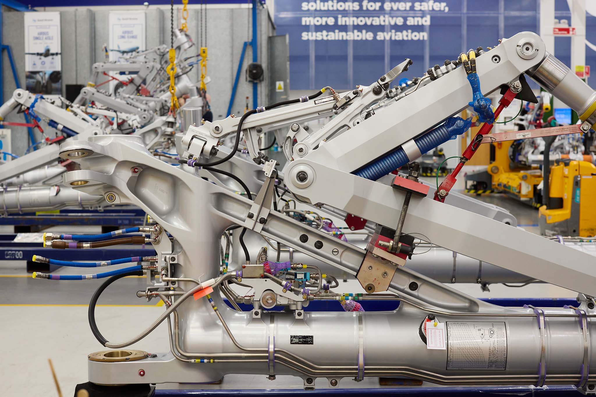 Safran Landing Systems inside of large factory with clear floors and high ceiling and strip lighting there are yellow steel metal machines and blue machines