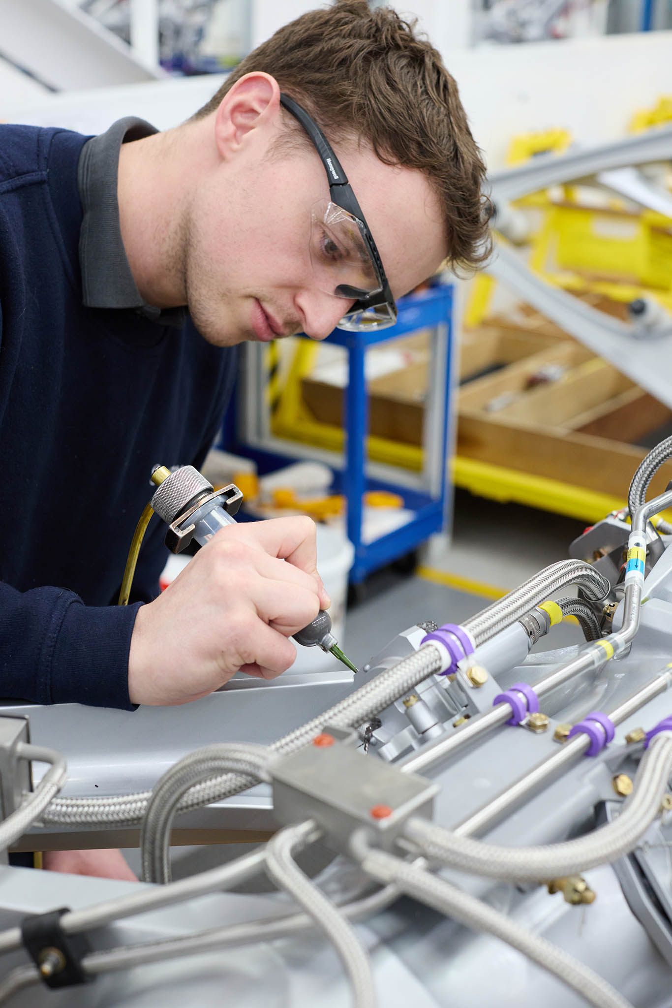 Safran Landing Systems engineer employee in protective glasses sitting at table desk working with tool on metal componentry pipes aircraft