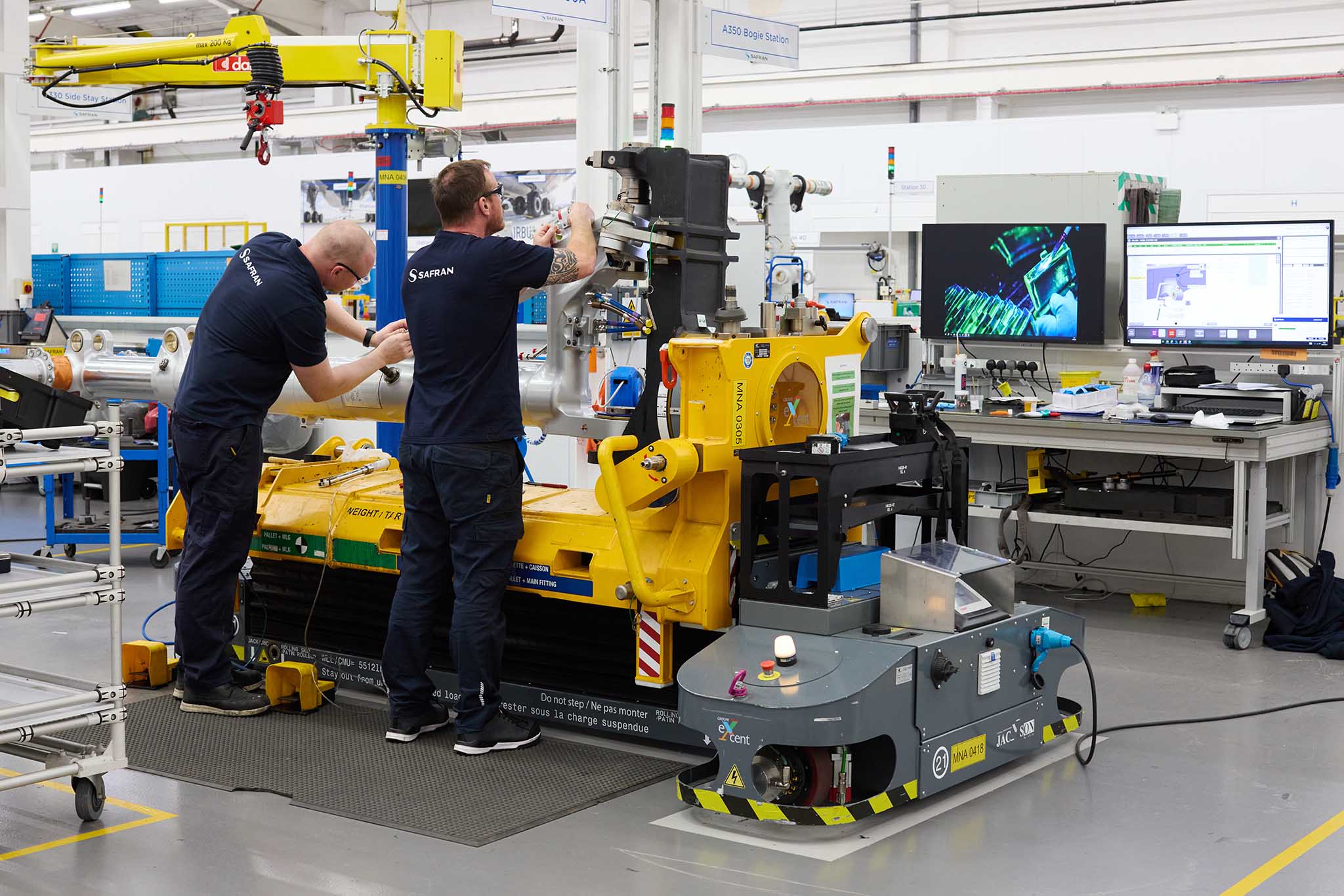 Safran Landing Systems two employees engineers in blue uniform working at yellow machine with screens in background