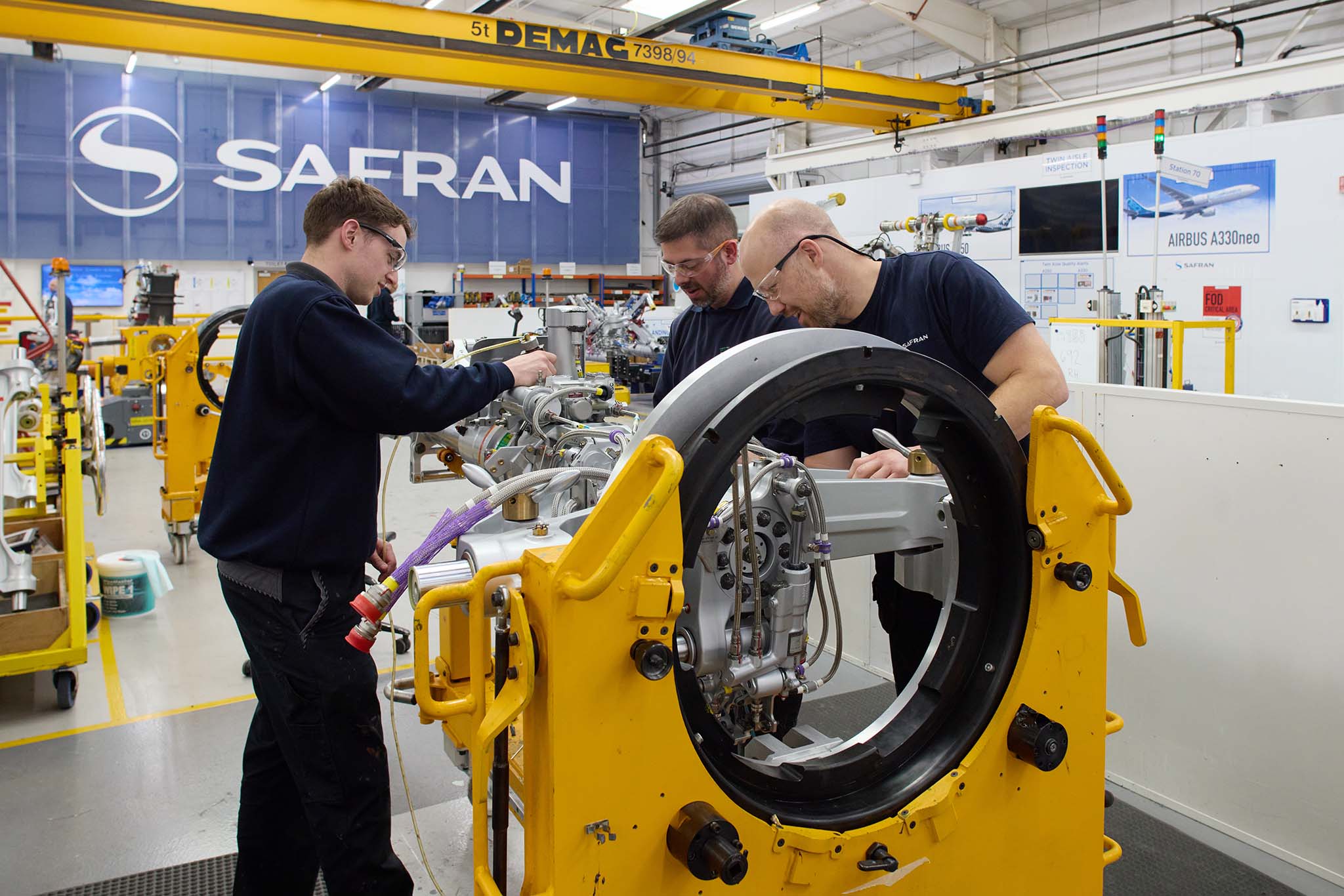 Safran Landing Systems engineers employee in protective glasses working with tool on large yellow metal componentry pipes aircraft