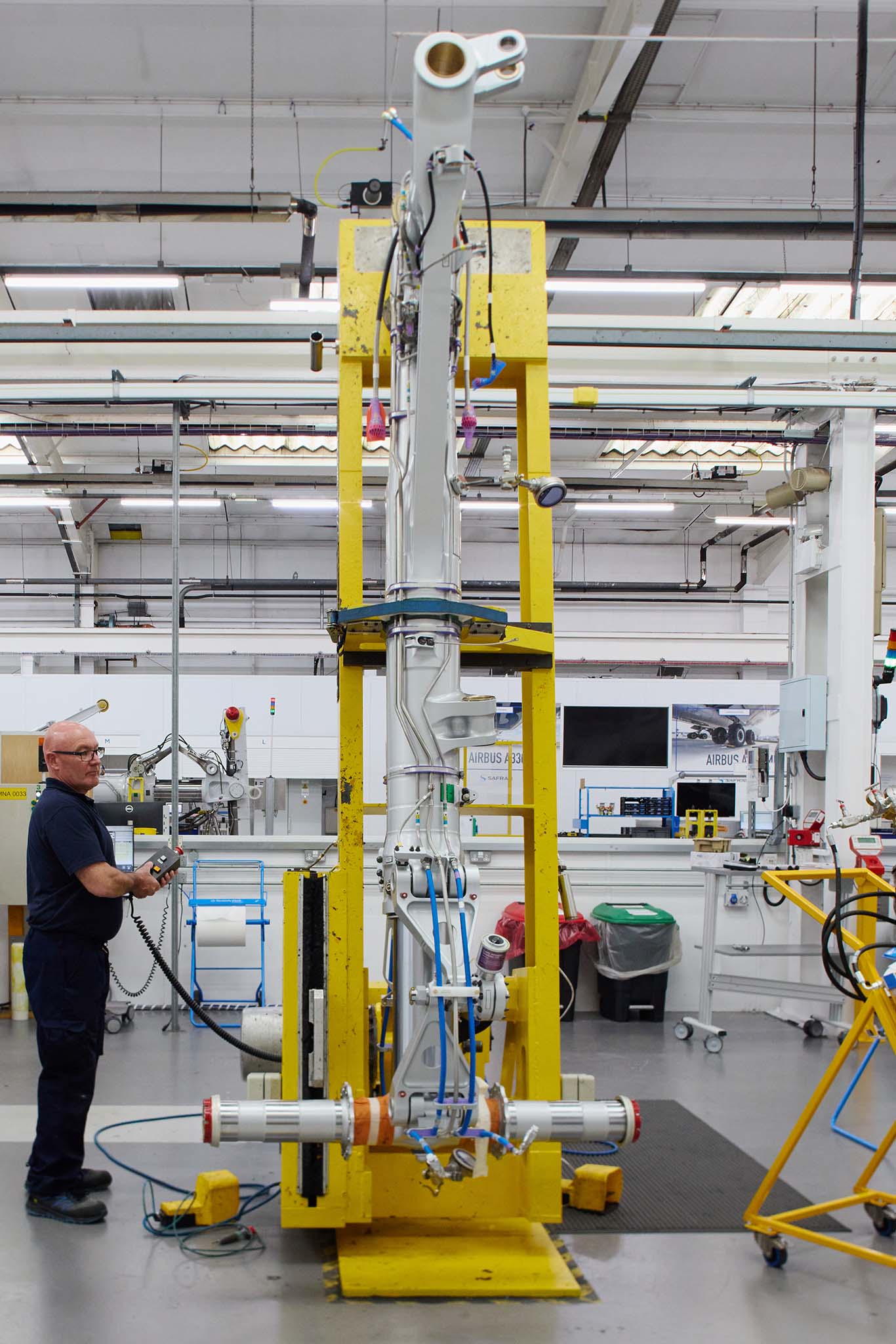 Safran Landing Systems inside factory building employee in uniform looking up at tall yellow machinery 