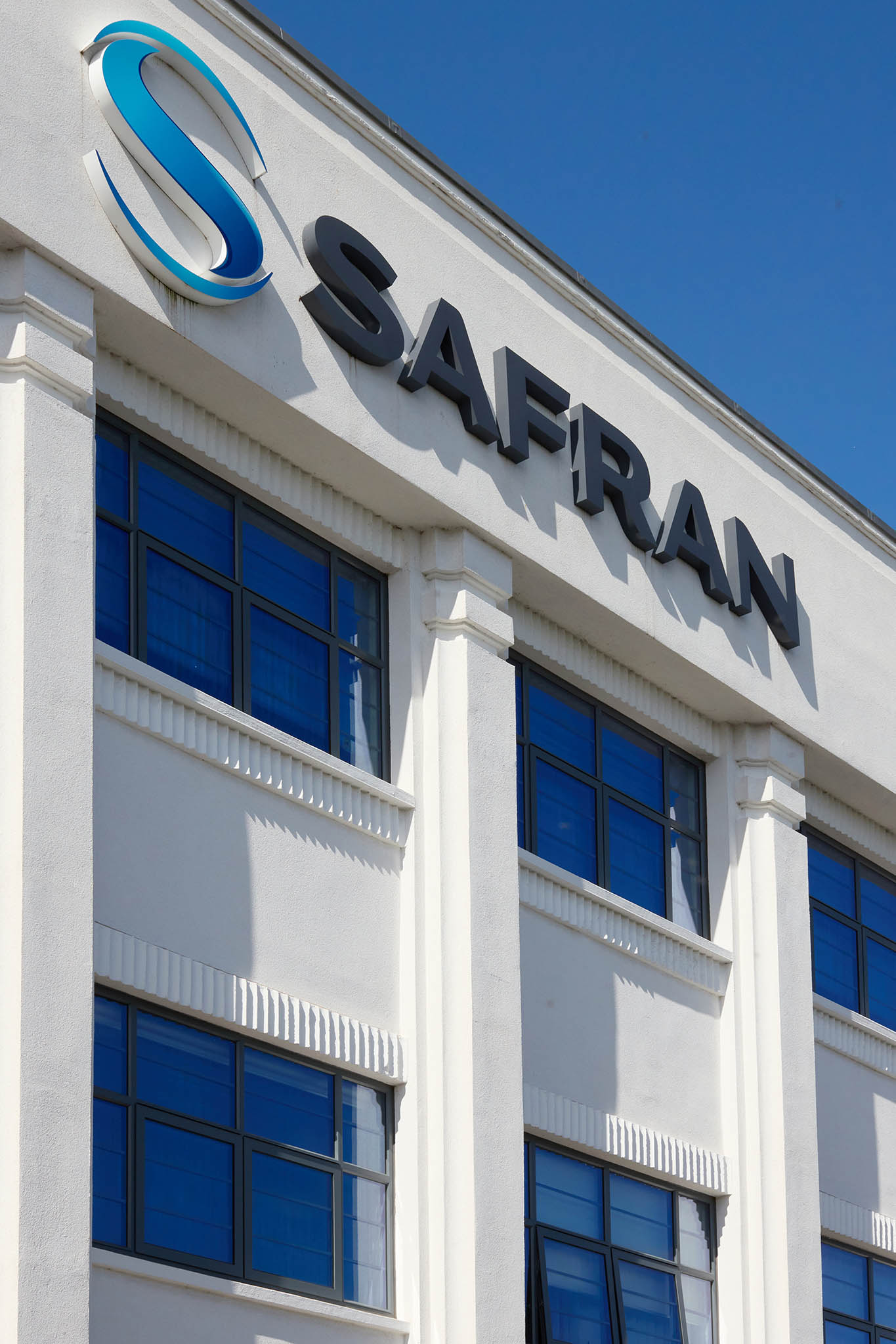 Safran Landing Systems outside factory building bright white with six blue windows the name of the company and logo is on the top of building in black letters the sky is blue