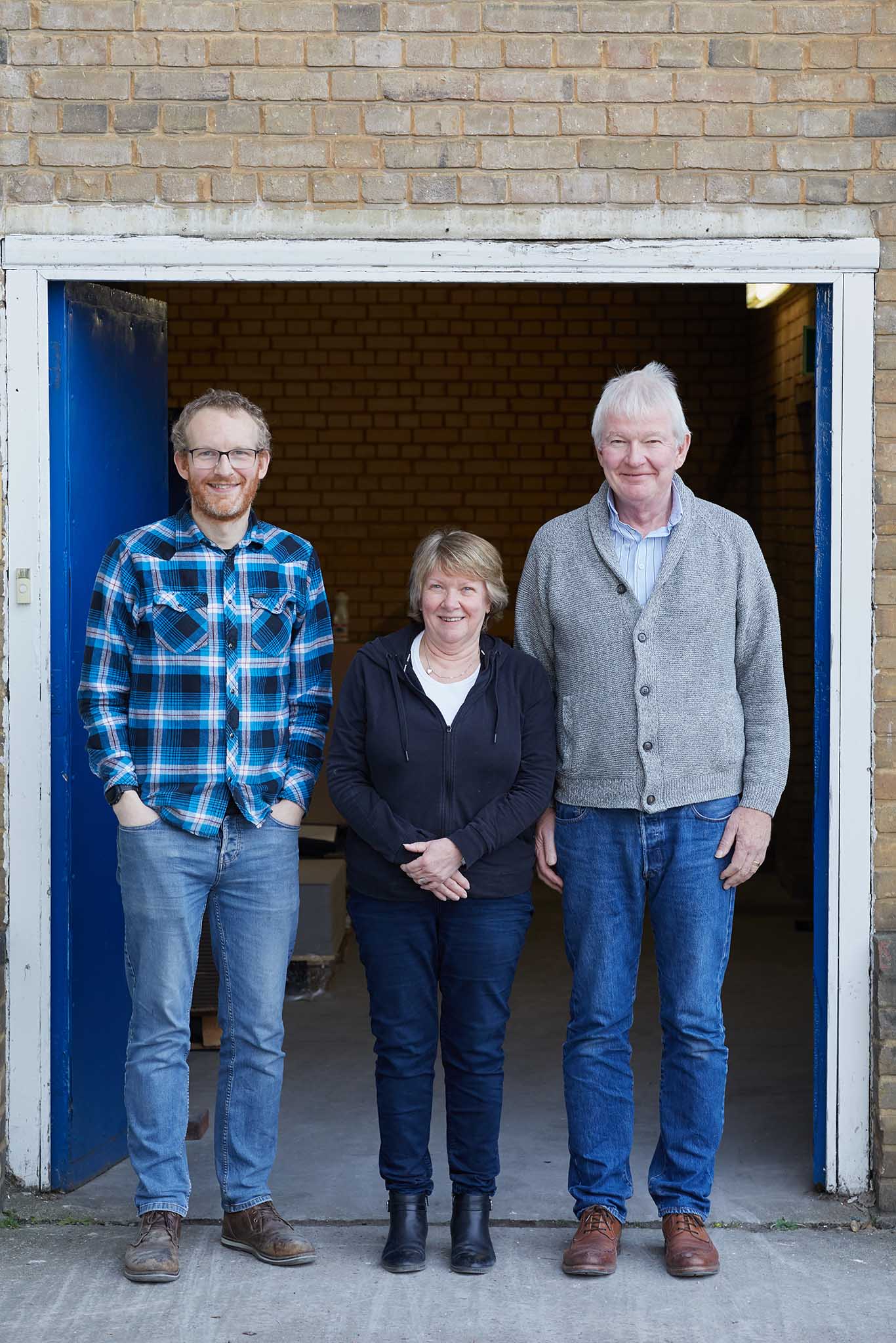 W MacCarthy & Sons two men standing either side of woman at open factory door all are smiling