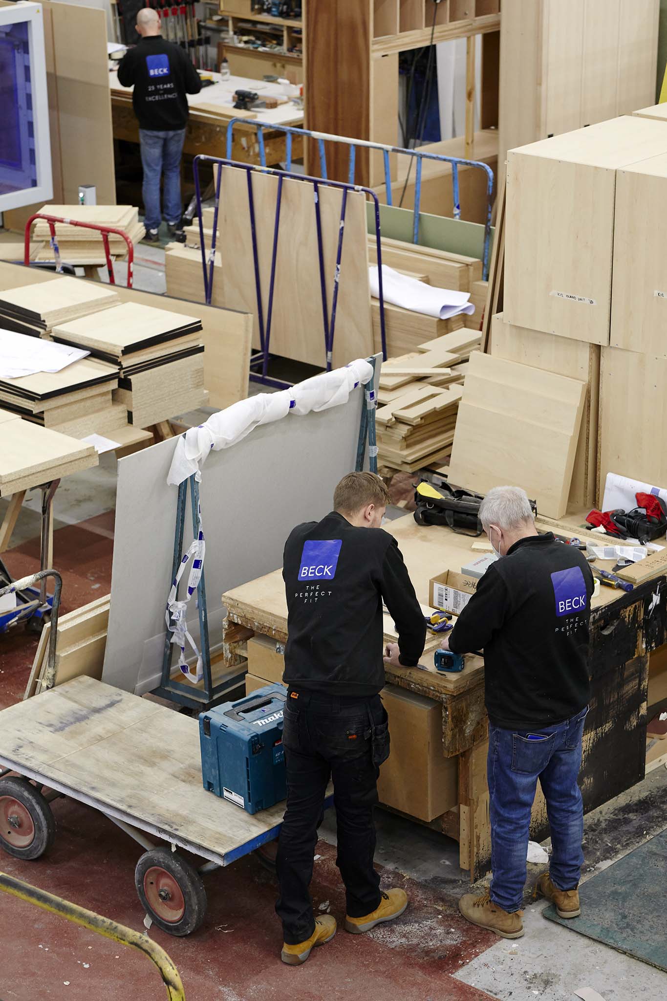 Beck large workshop floor taken from above two employee in dark uniform surrounded by light wood piled or leaning 