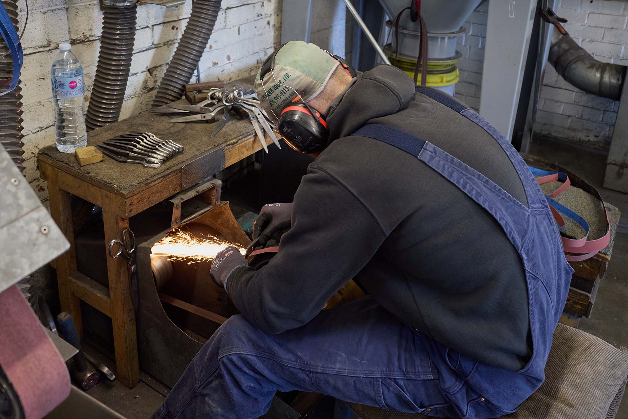 Ernest Wright man in blue workwear dungarees and protective welding mask  sitting at grinding wheel