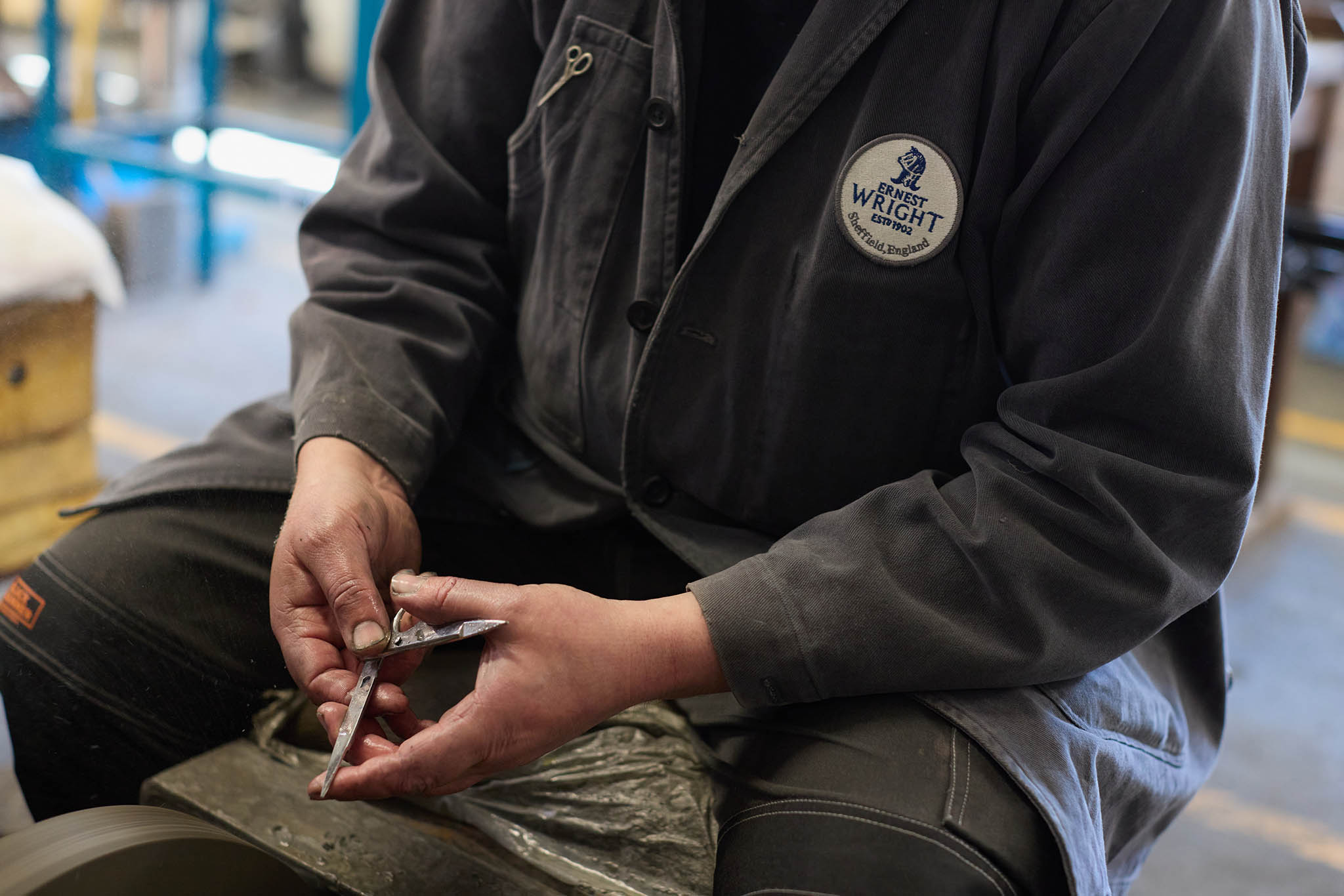 Ernest Wright man in dark grey black workwear sitting holding scissor shear making componentry