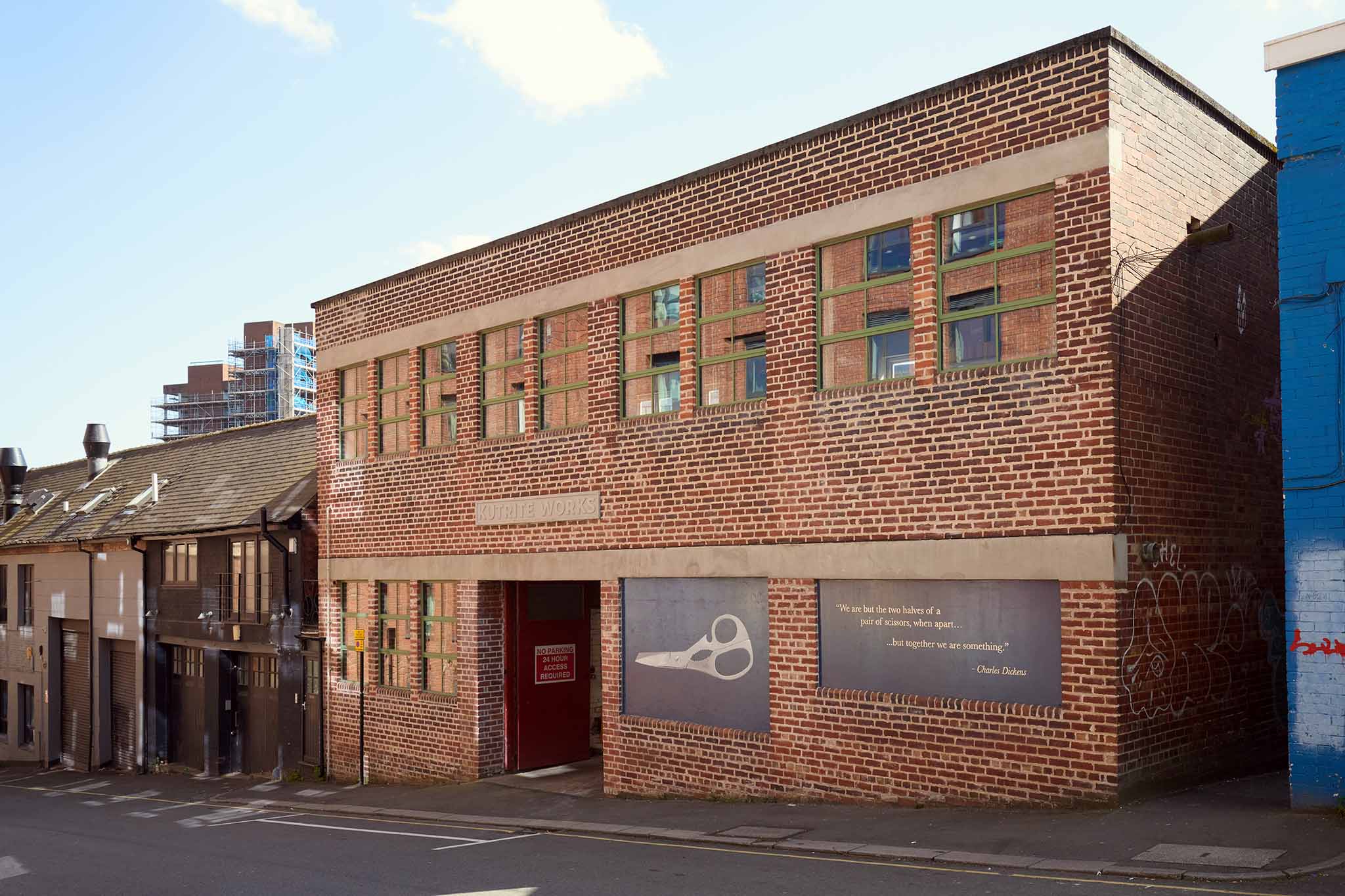 Ernest Wright red brick two storey factory building there are two large blue signs to the right of the building one has a pair of scissors painted on a blue background the other is writing