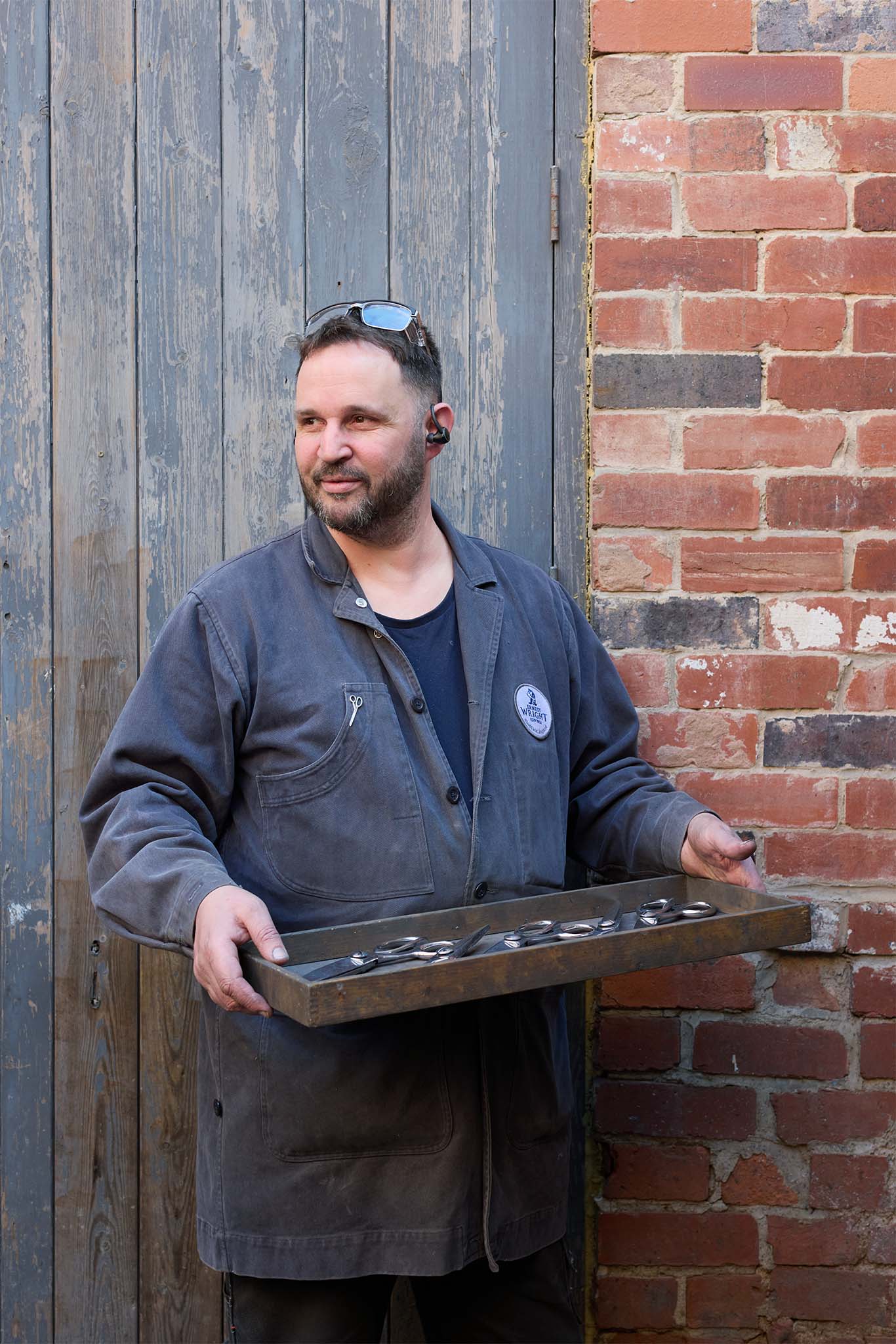 Ernest Wright man in blue work coat standing in front of wooden door red brick wall holding tray
