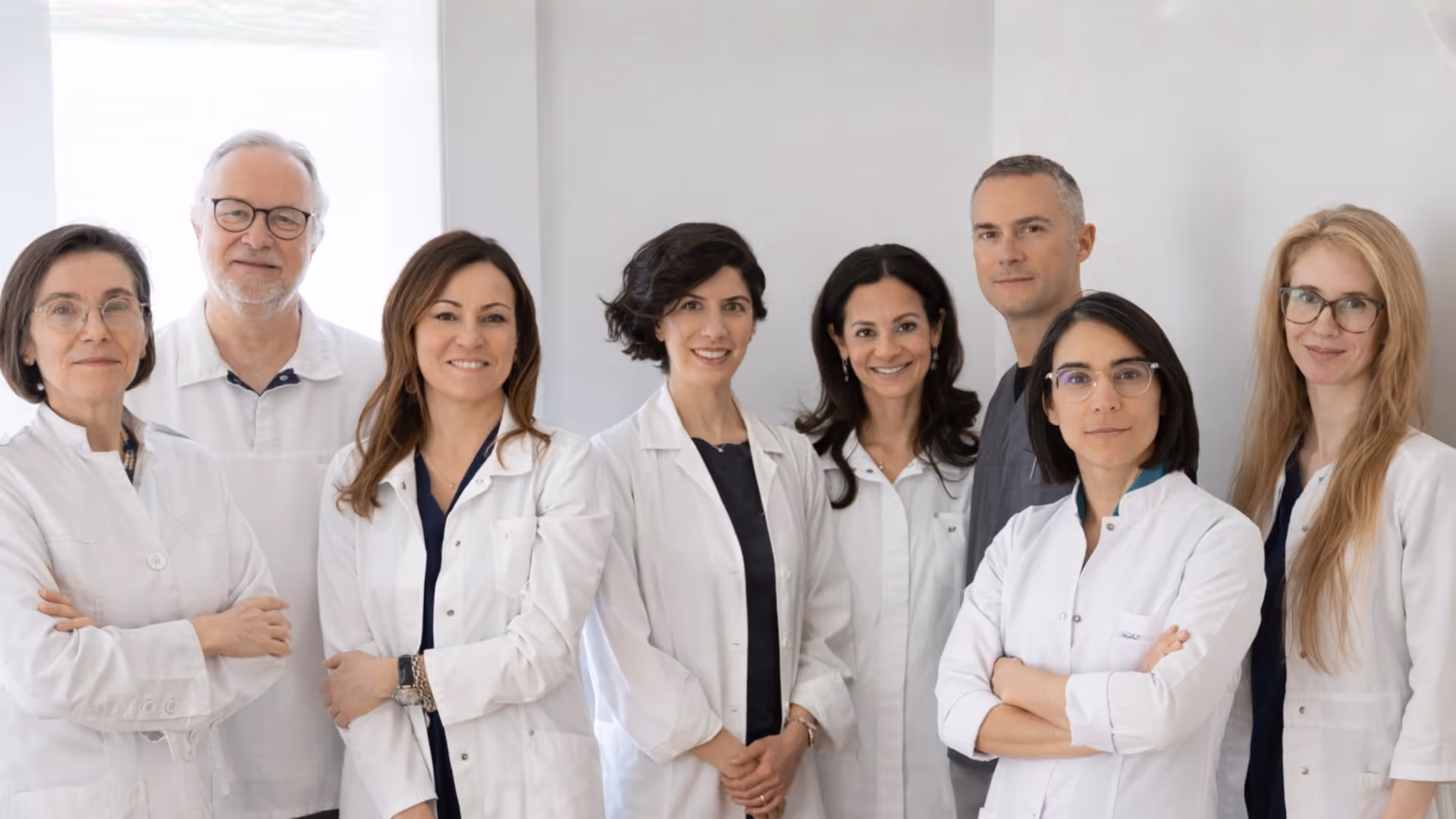 Groupe de sept professionnels de la santé en blouses blanches posant dans un environnement clinique.