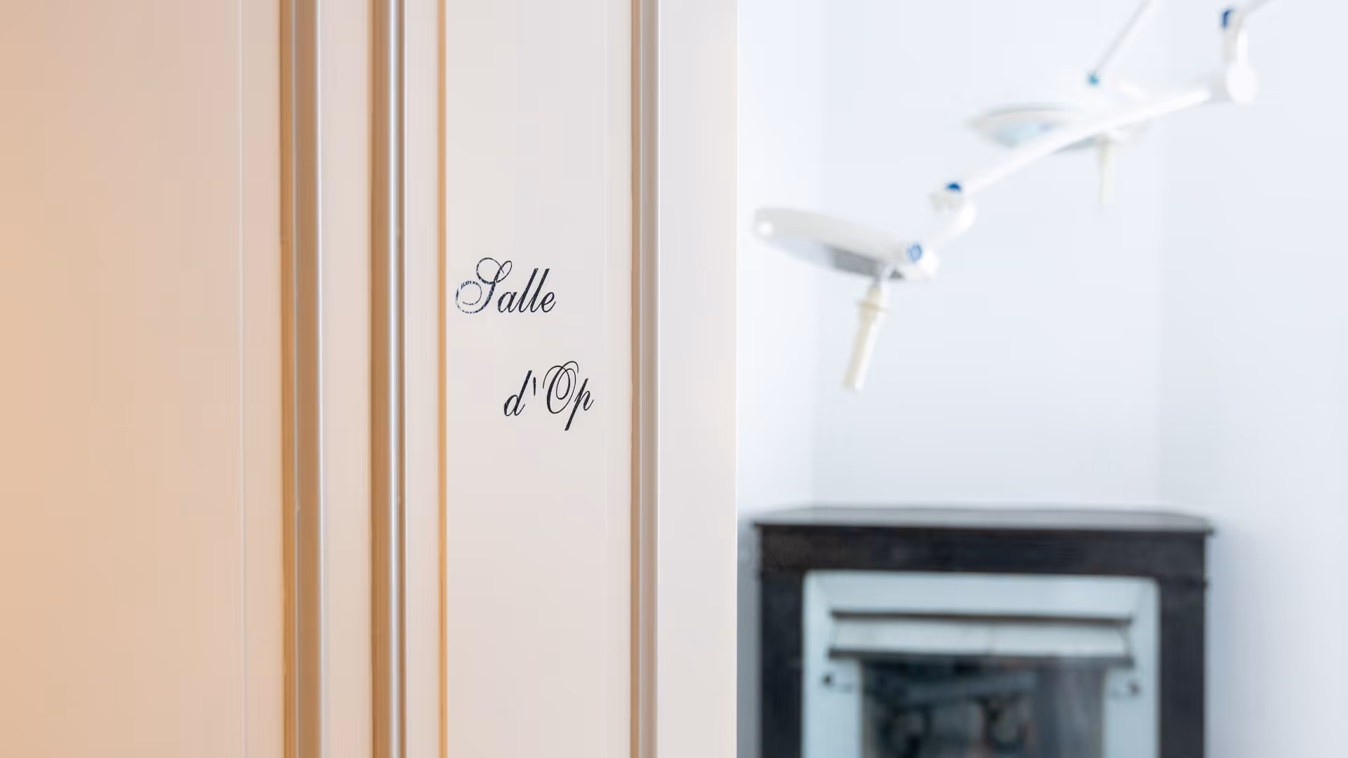 Porte blanche avec l'inscription « Salle d’Op » à côté d’un mur clair et un appareil médical suspendu.