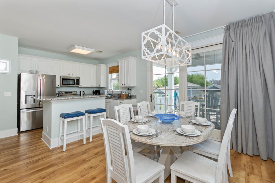 Bright coastal dining area and kitchen with white cabinets, stainless steel appliances, breakfast bar, and table set for six at a North Myrtle Beach vacation rental.