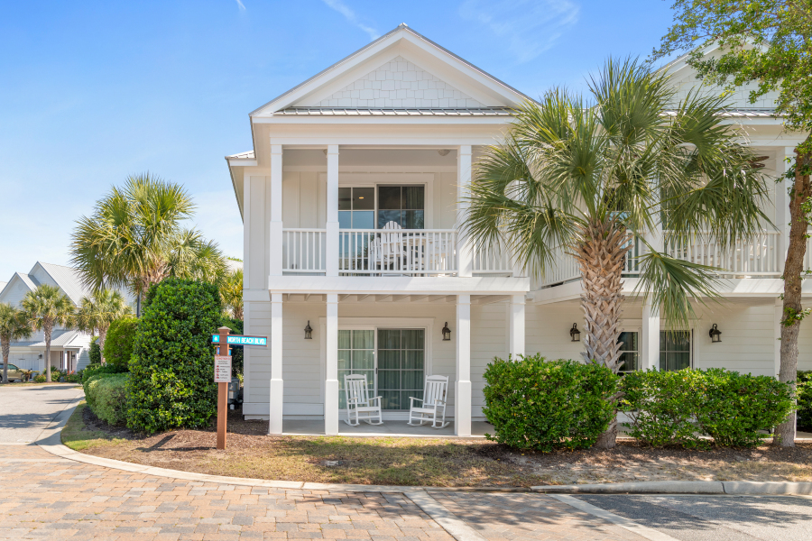Exterior of a white coastal vacation home with double porches, palm trees, rocking chairs, and a North Beach Resort sign in North Myrtle Beach.