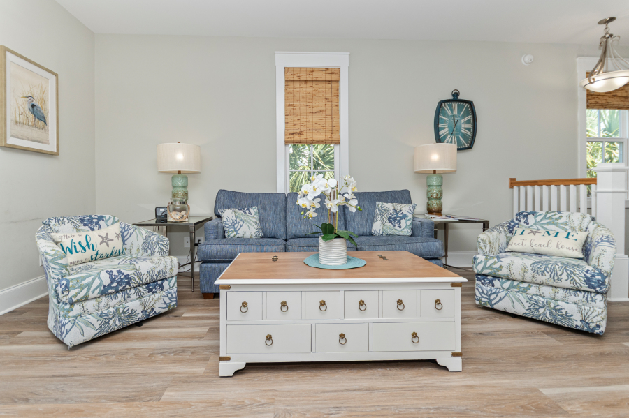Coastal living room at the Sandpiper vacation rental with blue sofa, patterned accent chairs, beach decor, and white coffee table in North Myrtle Beach.