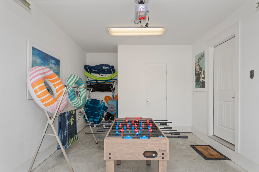 Garage game and beach gear area with a foosball table, pool floats, beach chairs, towels, and outdoor equipment stored neatly for guest use.