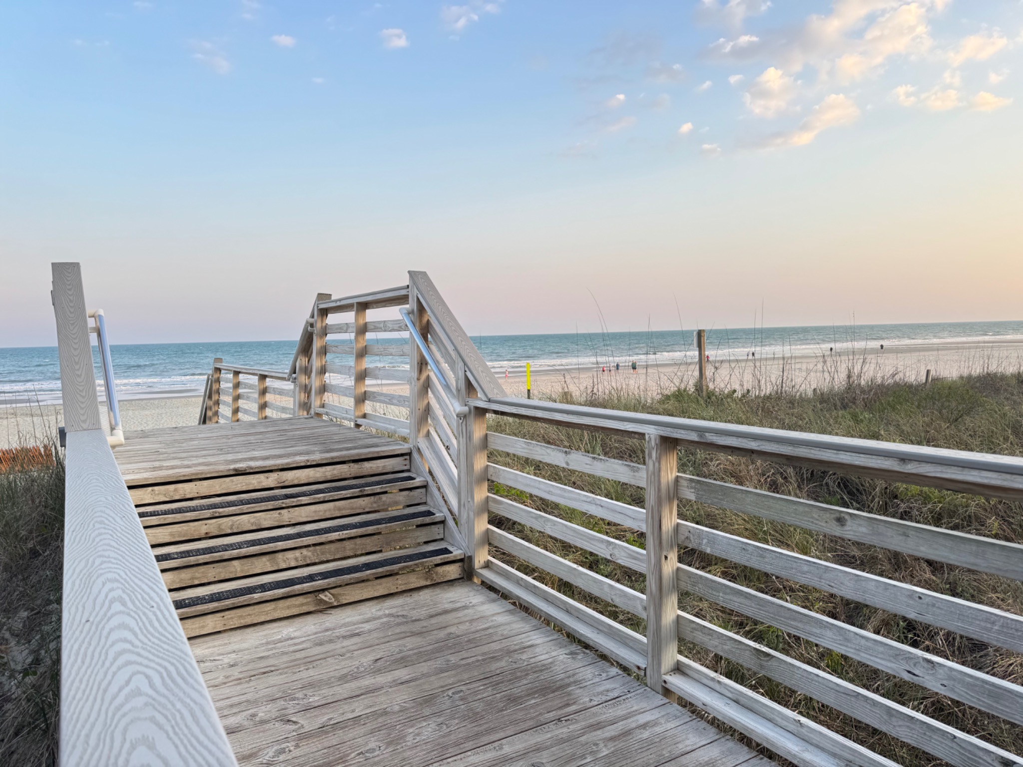 Wooden beach access boardwalk leading over the dunes to the ocean at sunset.