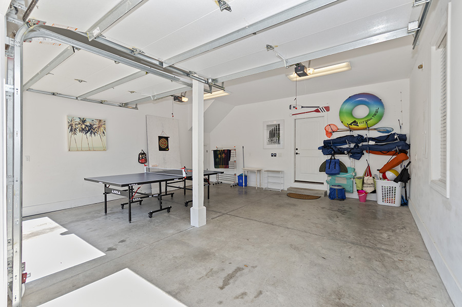 Garage game and beach gear area with a foosball table, pool floats, beach chairs, towels, and outdoor equipment stored neatly for guest use.