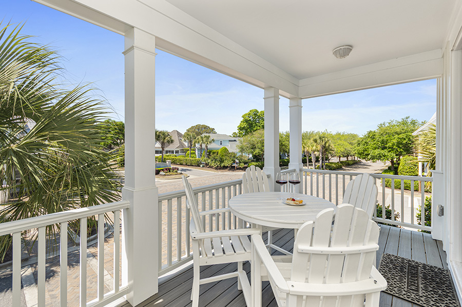 Covered balcony with white Adirondack chairs, round table, beach towel, drinks, and neighborhood views at a North Myrtle Beach vacation rental.