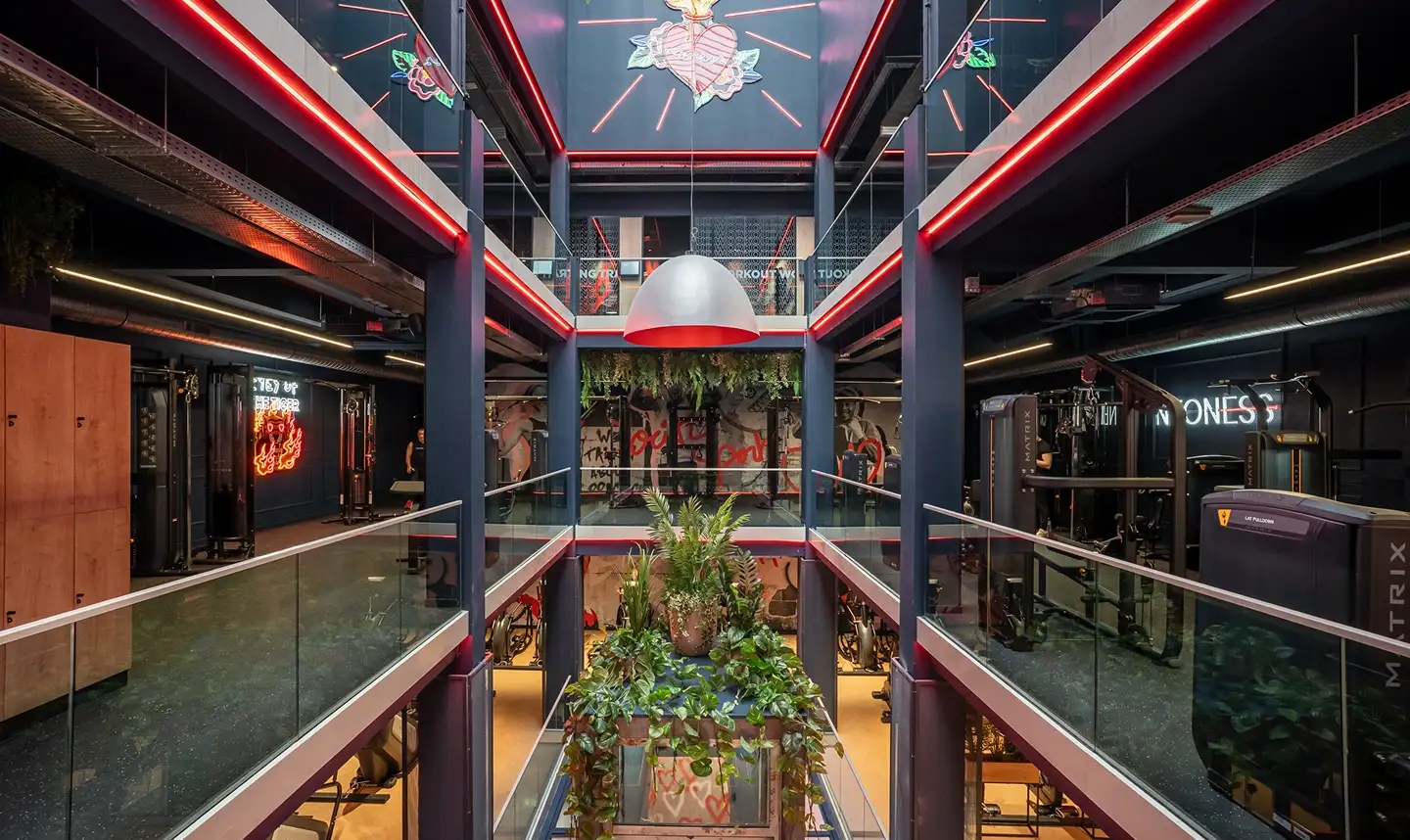 Intérieur moderne de salle de sport avec plantes au centre, équipements de musculation et éclairage LED rouge.