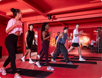 Groupe de cinq personnes faisant des exercices en tapis dans une salle de sport avec des murs rouges.