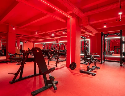 Salle de musculation avec équipements variés, murs et sols rouges, plusieurs machines de fitness disposées dans la pièce.
