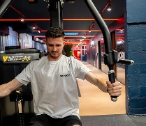 Homme s'entraînant avec une machine de musculation dans une salle de sport moderne au sol en bois clair.