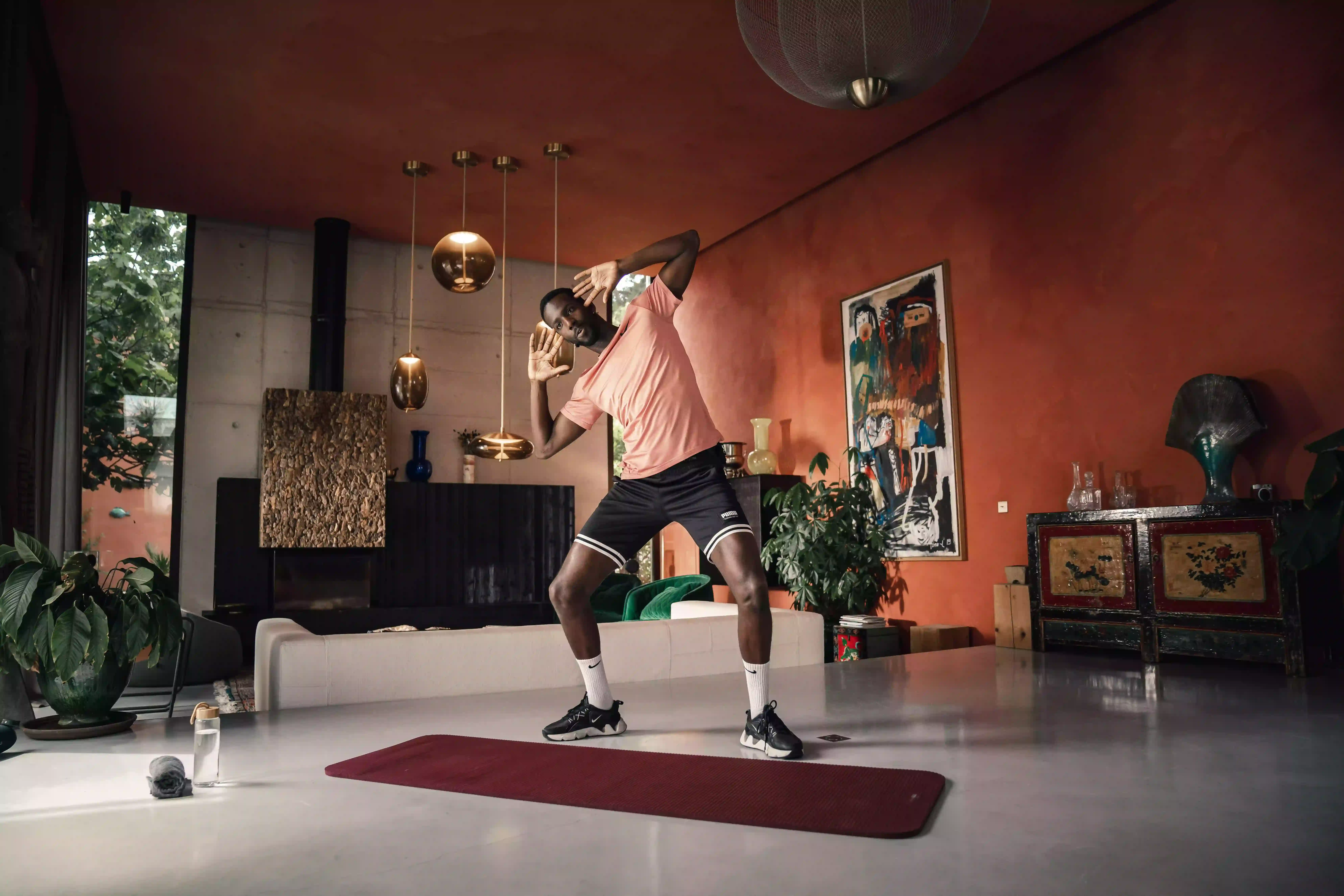 Homme s'entraînant sur un tapis de yoga rouge dans un salon moderne avec murs orange et décoration contemporaine.