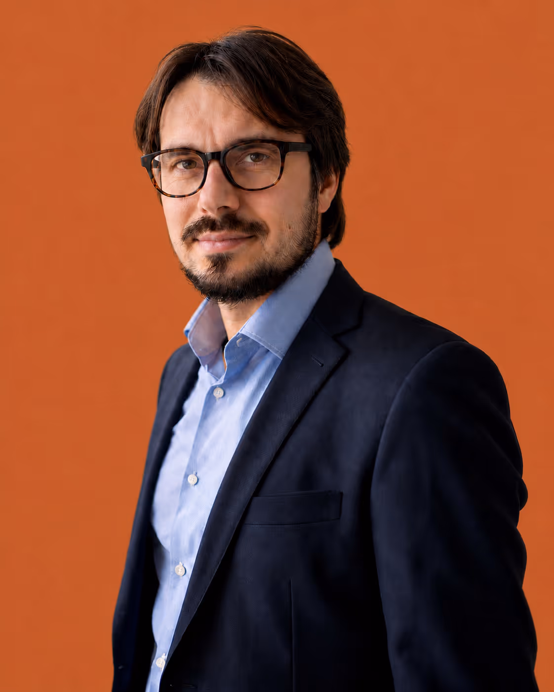 Jacopo Francia. Man in glasses wearing a dark blazer and blue shirt, posing with a slight smile against a beige background.